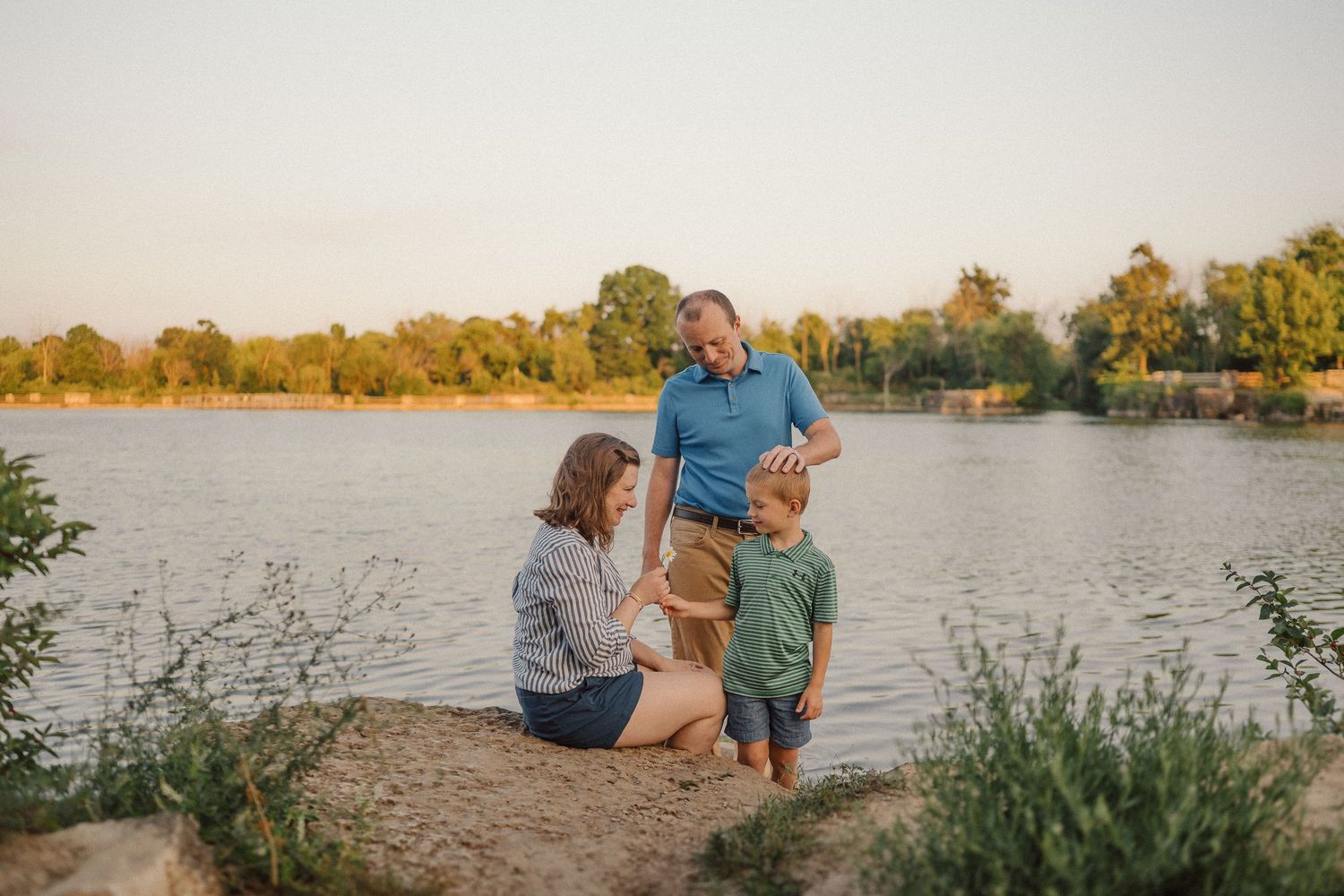 Family sharing a tender moment together by a serene lakeside at golden hour.