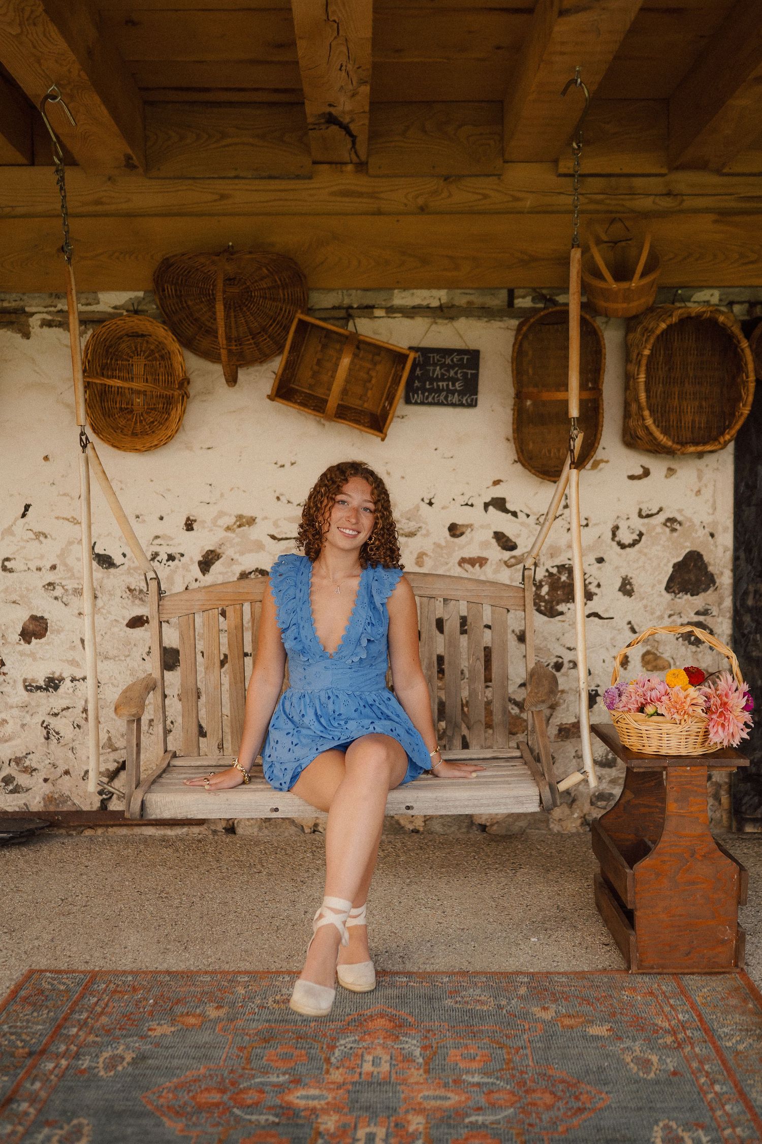 Person in blue eyelet top poses on vintage patterned rug in rustic barn setting with wooden decor.