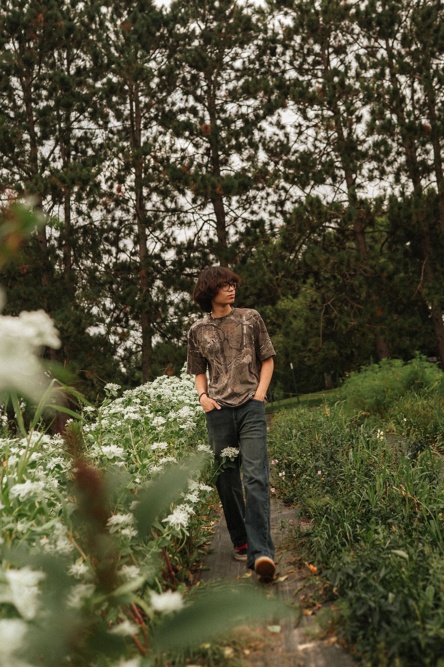 A person walking through a lush garden path with blooming flowers and greenery on a summer evening.