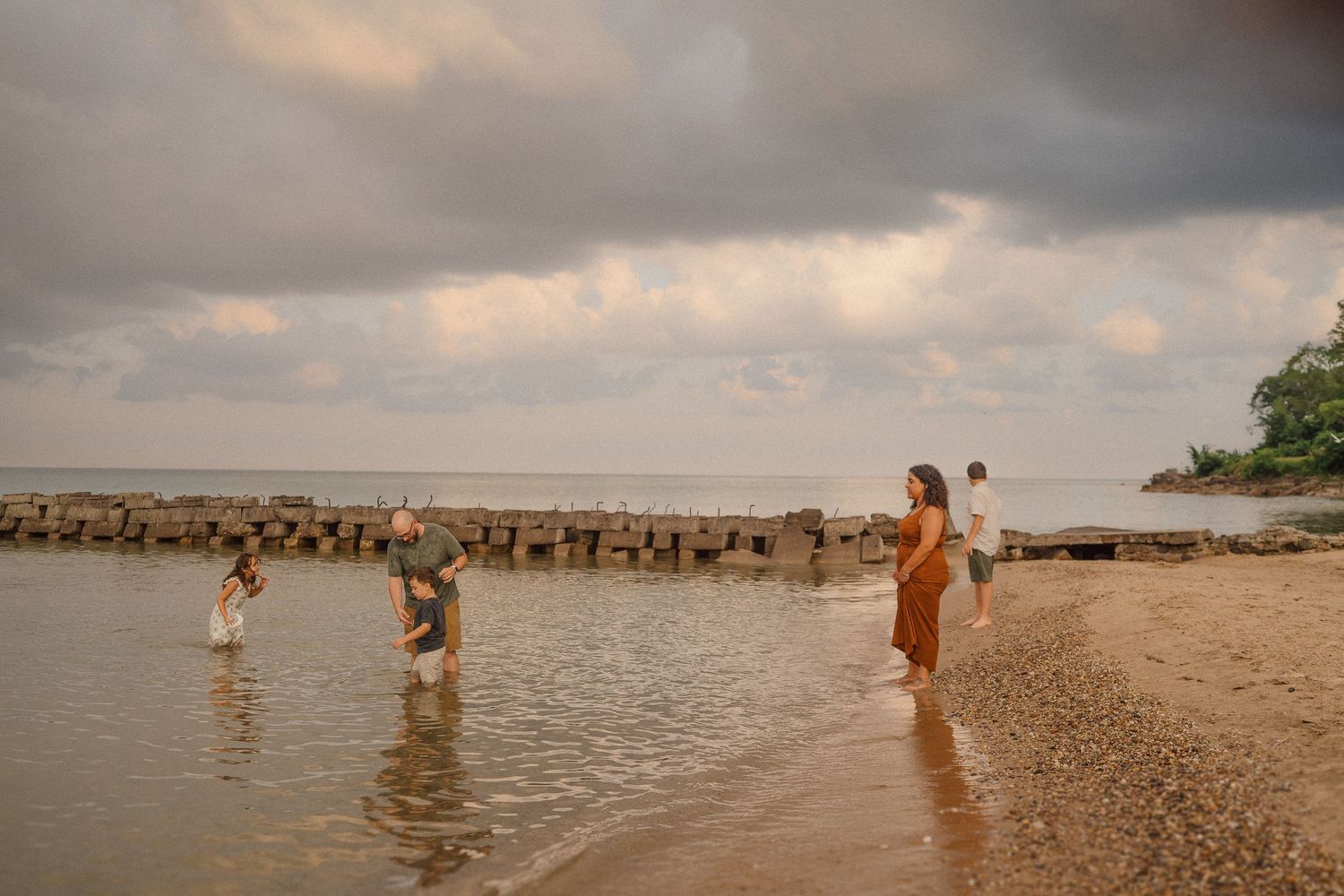 A series of silhouettes play in shallow ocean waters during a moody sunset along the shoreline.