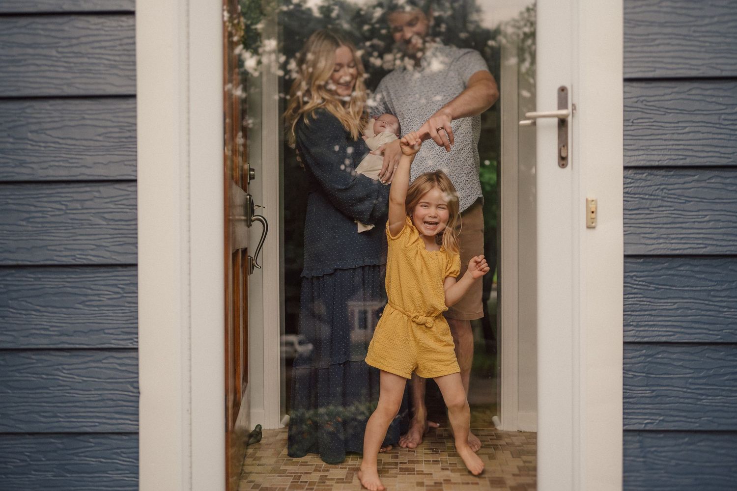 A joyful child in yellow plays in a white doorframe of a blue house.