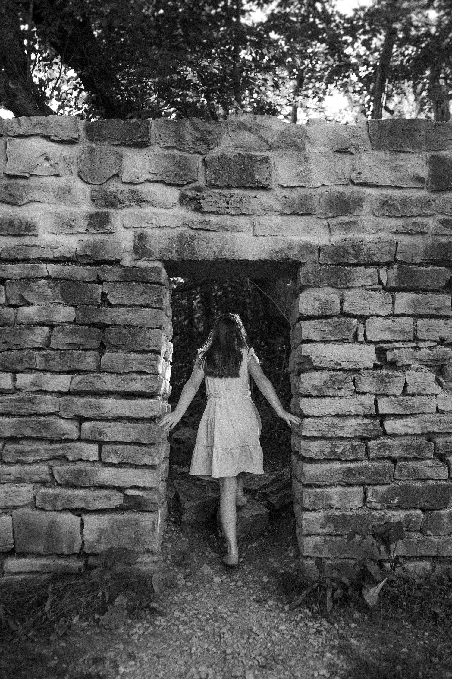 A sequence of four black and white photos showing a figure in white dress disappearing gradually through a stone wall opening.