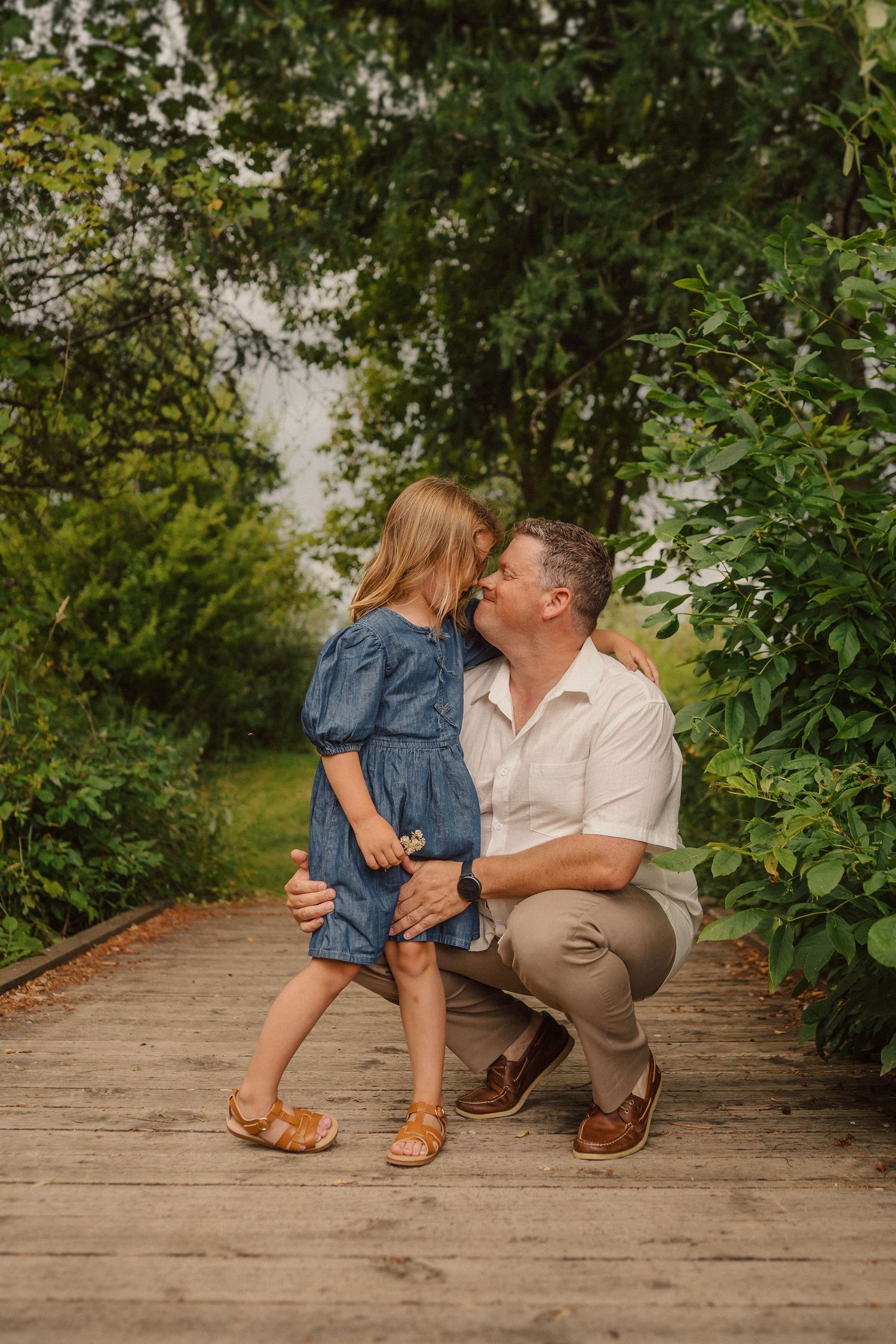 Parent and child share tender moment while crouching on wooden bridge path.