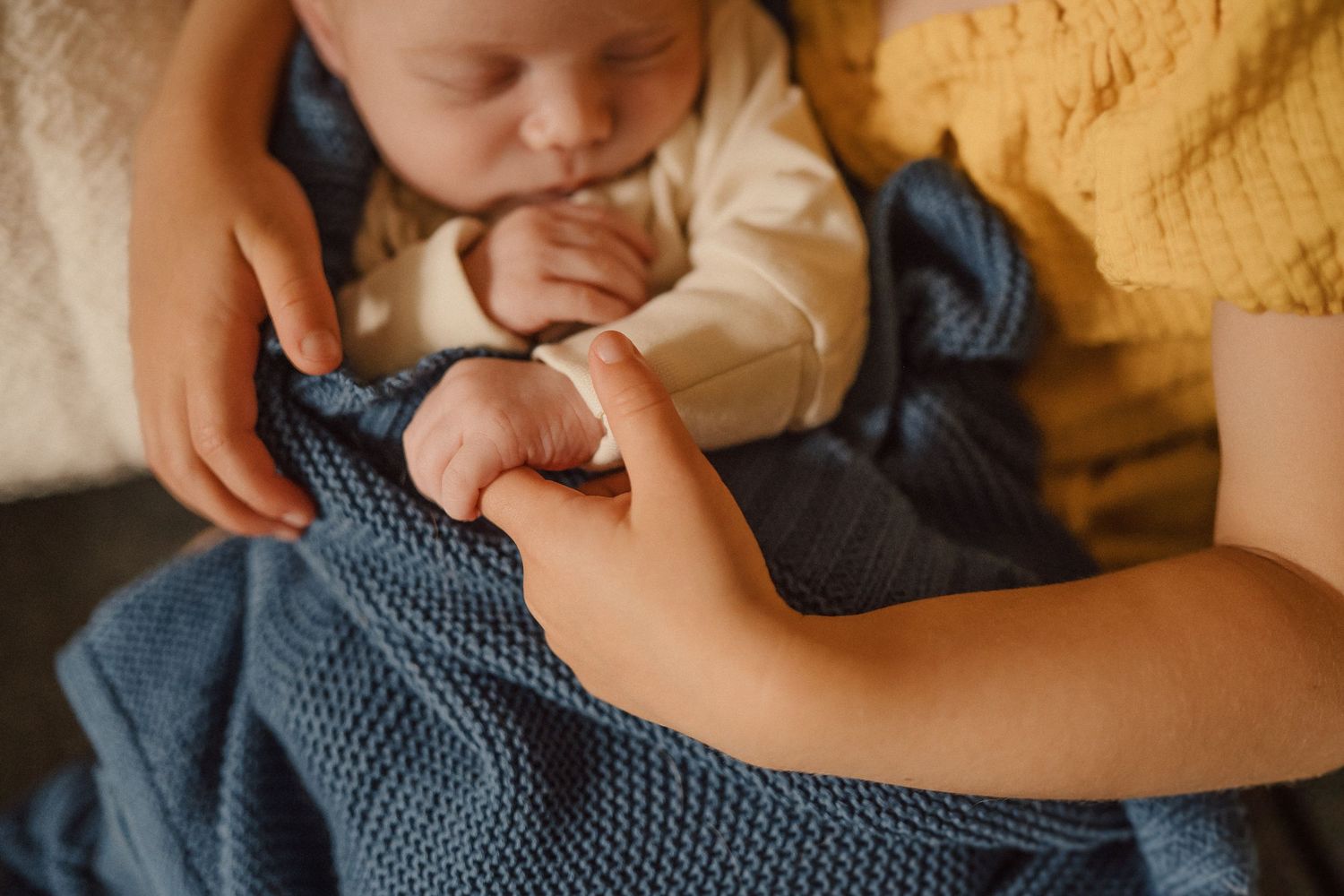 Close-up detail of tiny infant hands being gently held against a blue blanket.