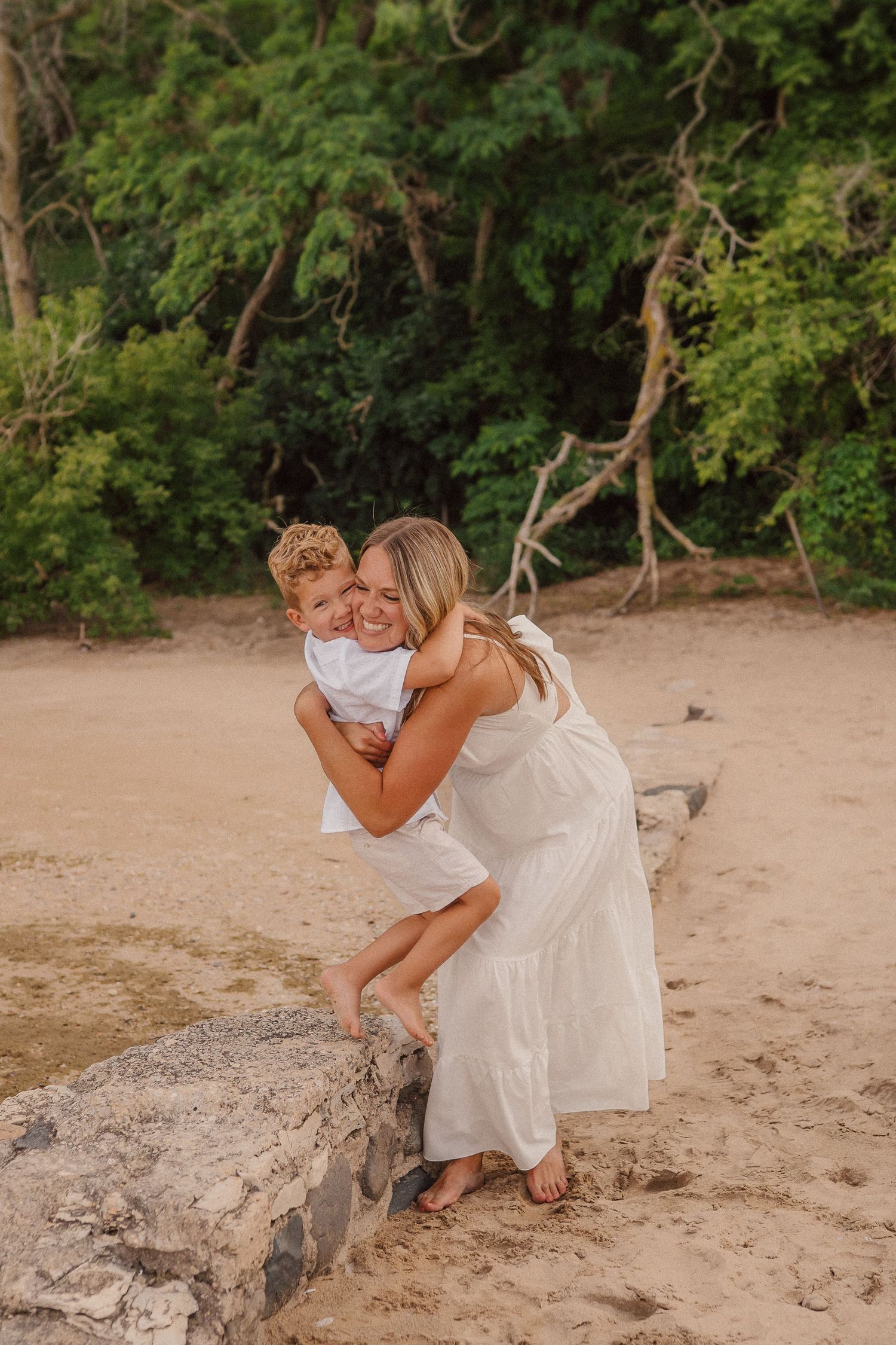 A tender moment shared on a sandy beach with lush tropical trees in the background.
