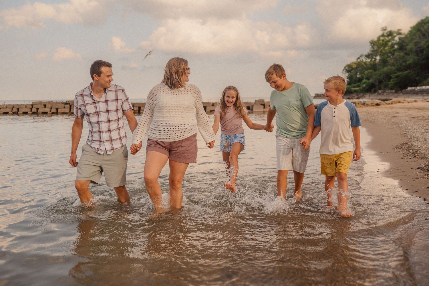 A group walks together through shallow ocean water at sunset along a peaceful beach.