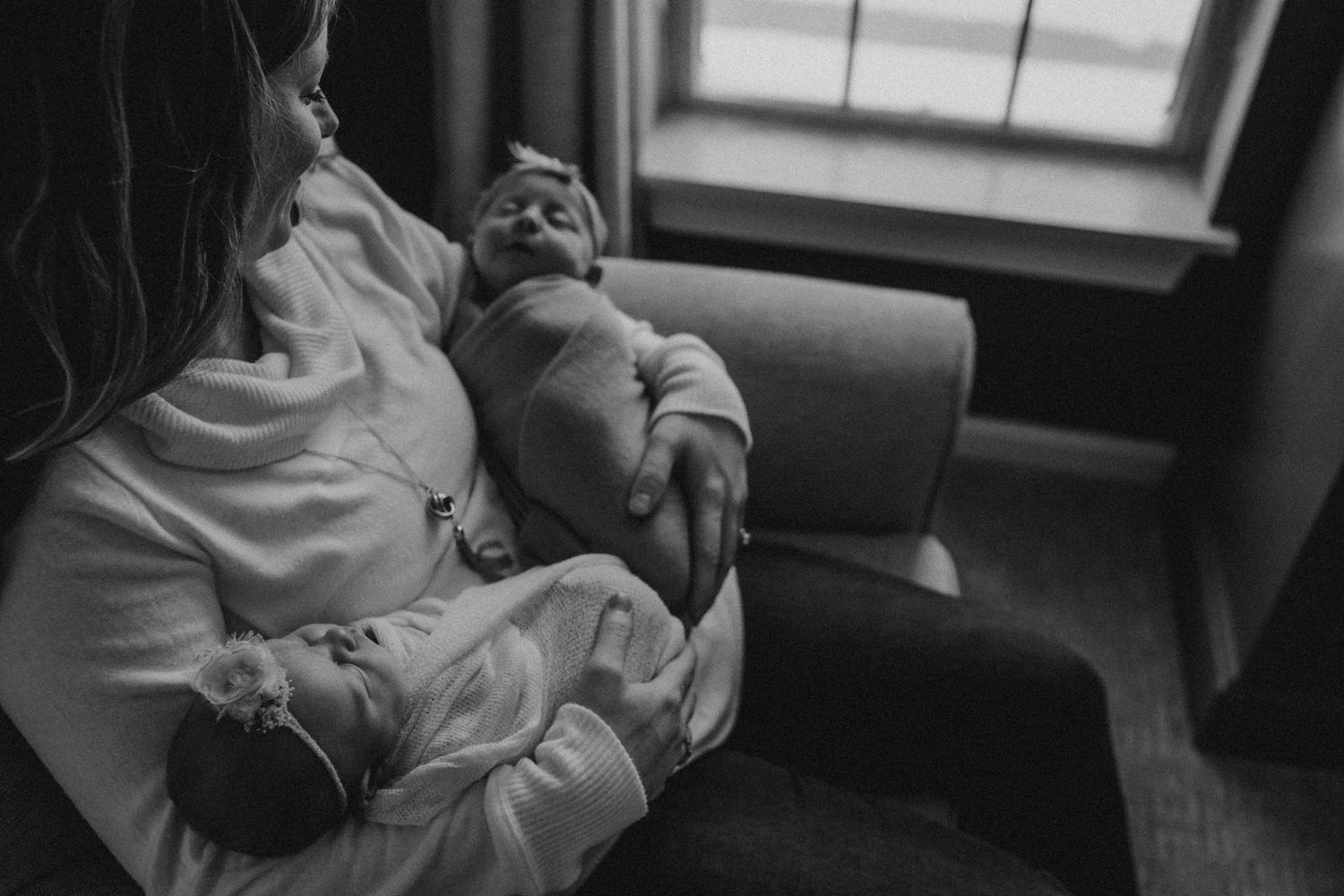 Tender moment of parent and newborn baby relaxing together on a couch in black and white.