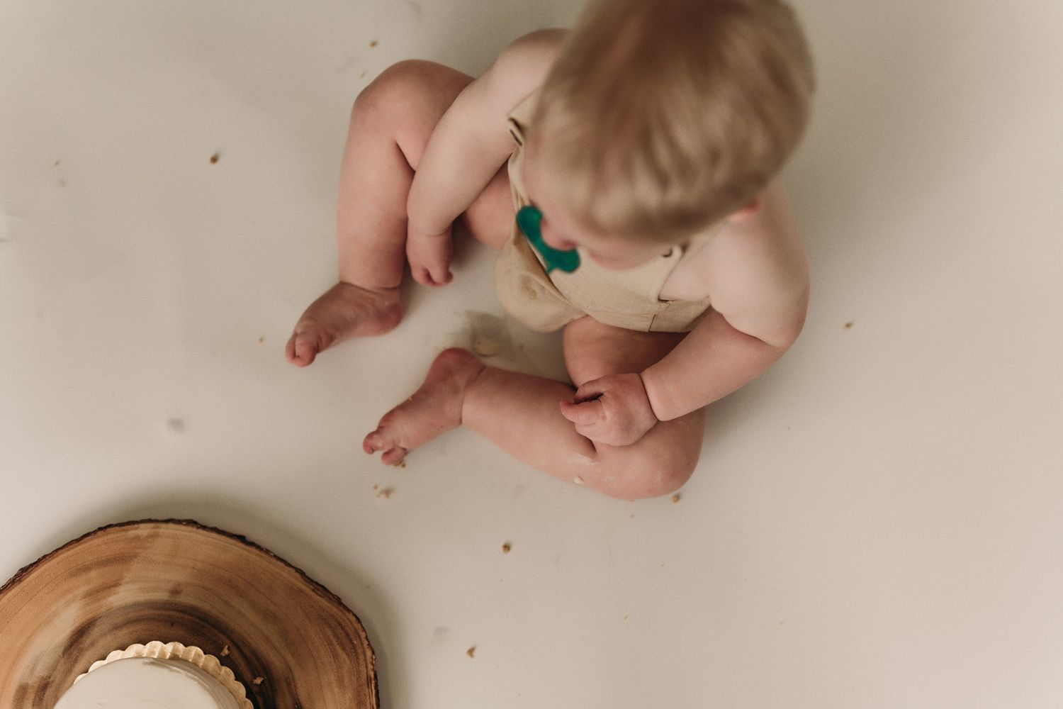 Overhead view of infant exploring wooden coaster with cup during minimalist photography session.