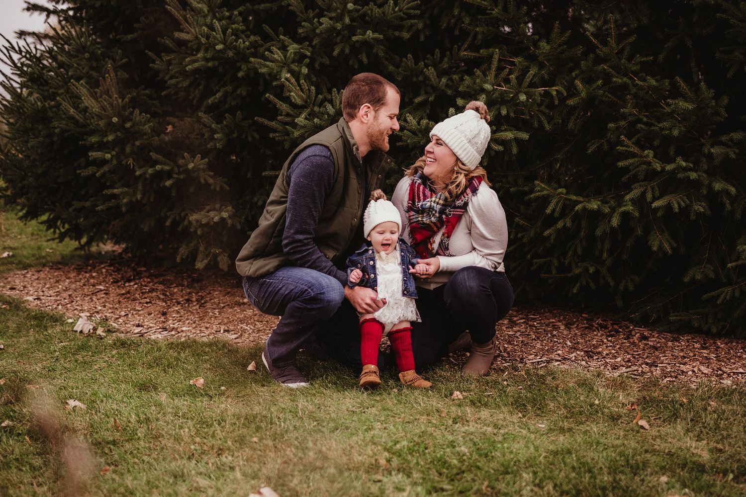 Family kneeling together outdoors with toddler in red boots during winter season.