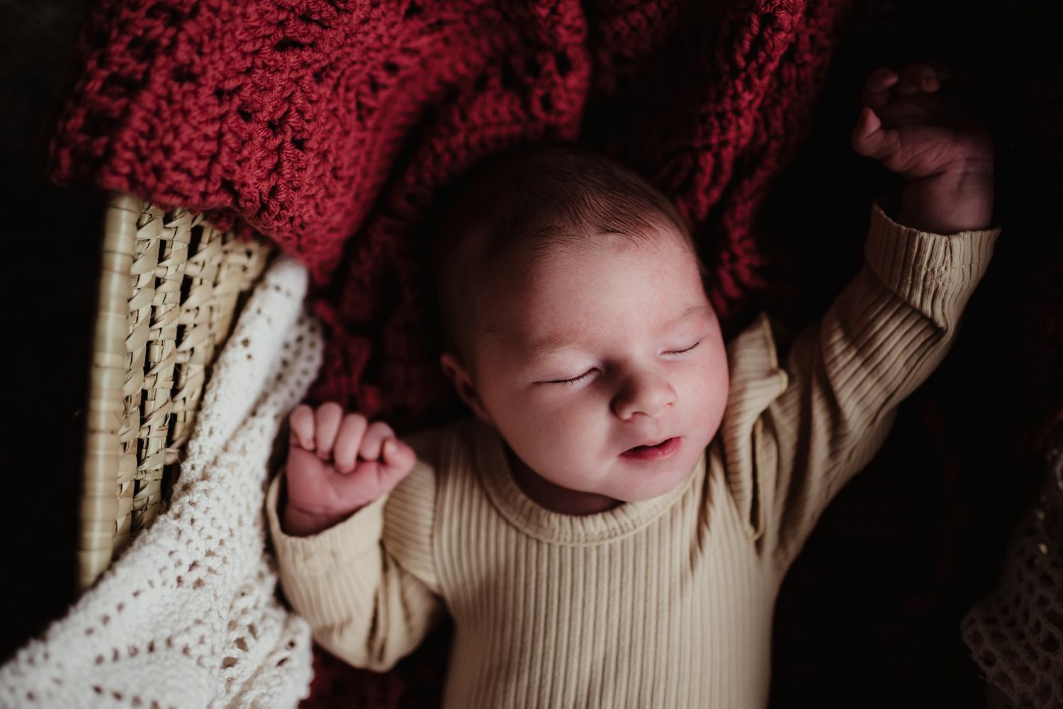 Sleeping newborn in cream sweater lying on red and white knit blankets.
