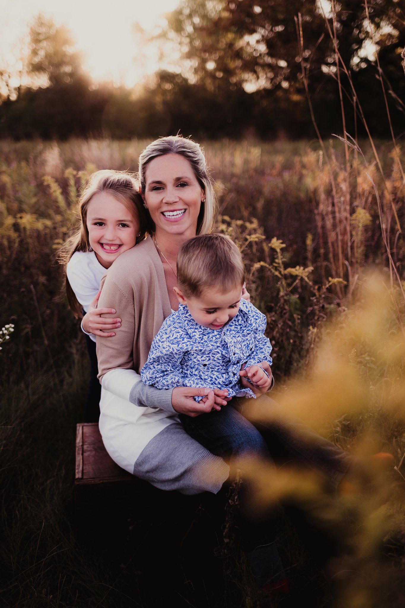 Family portrait in golden sunlit meadow with tall grass and warm autumn tones.
