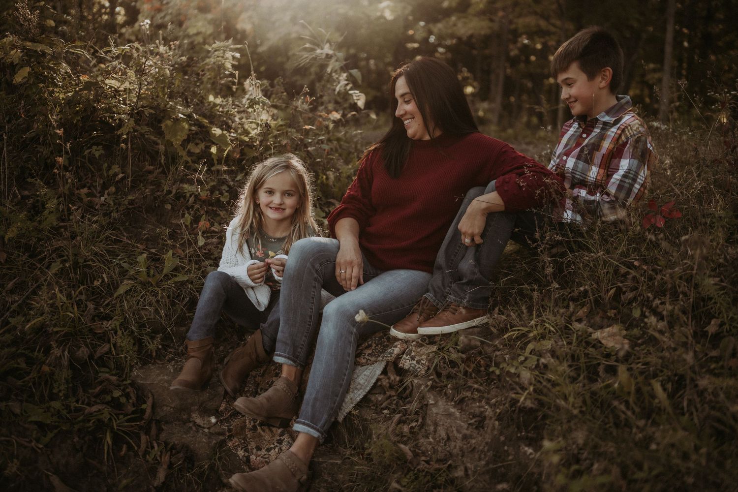 Casual family portrait session on grassy hillside with warm autumn lighting.