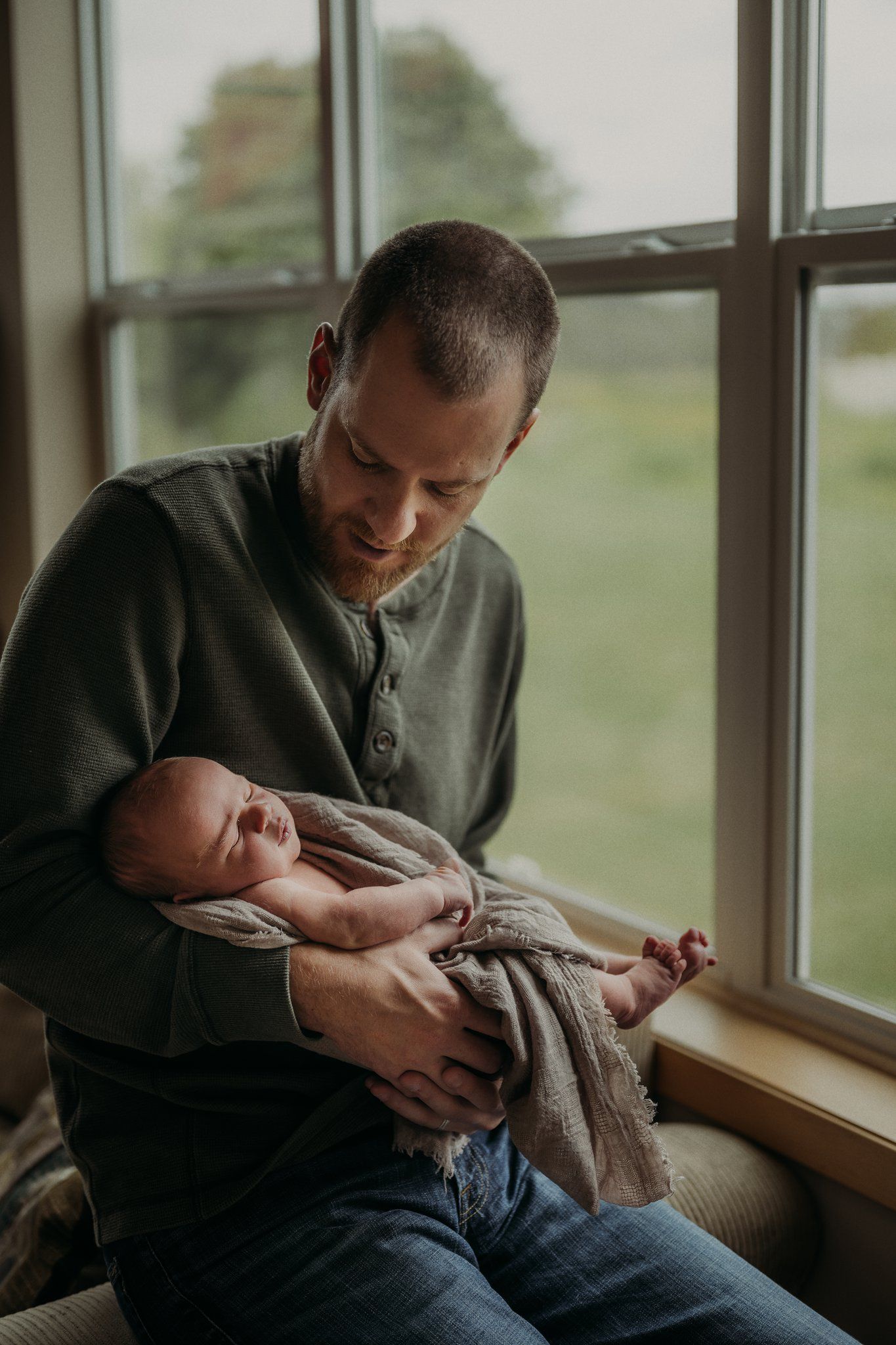 Tender moment between parent and sleeping infant by window.