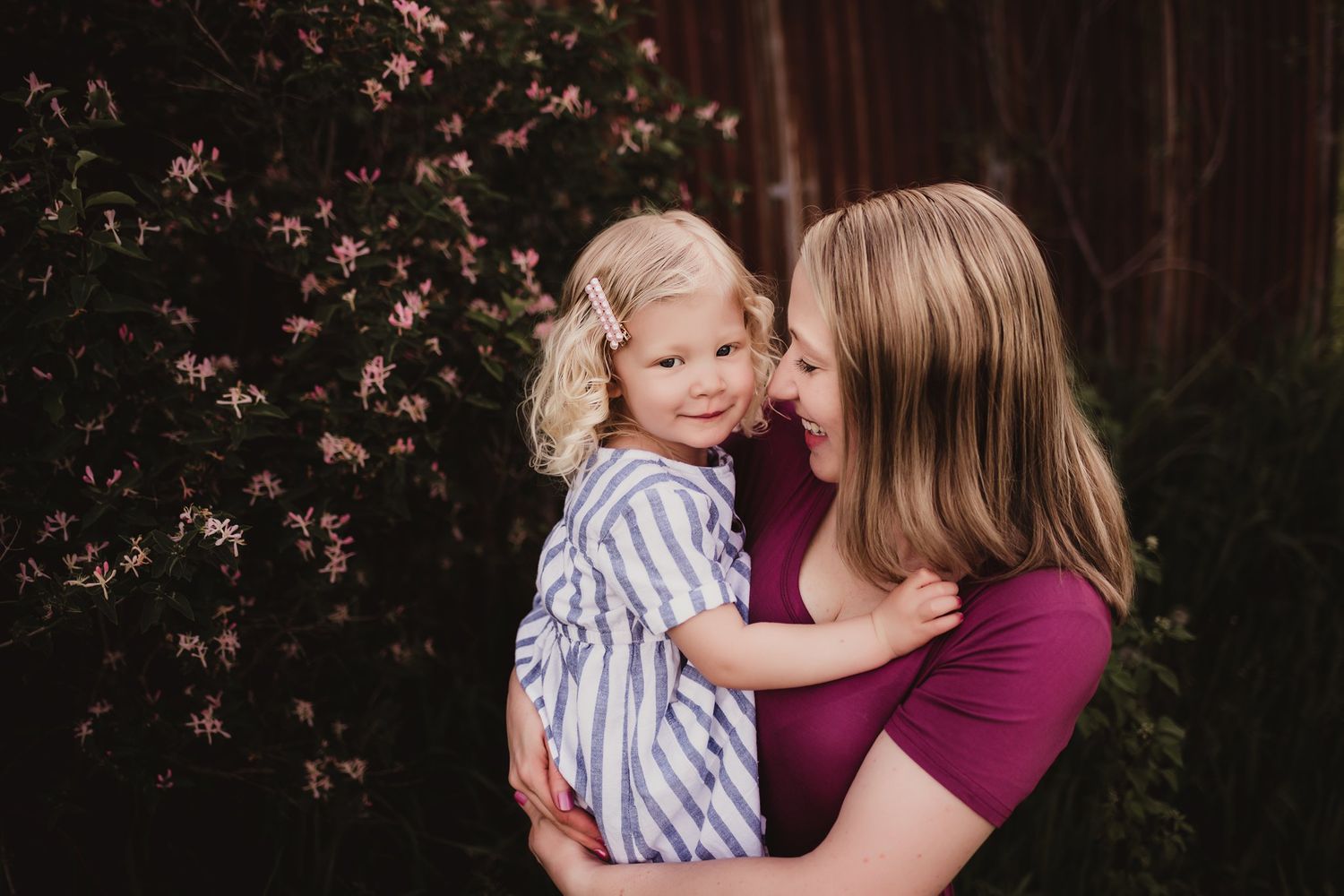 Sweet moment captured against flowering bushes with burgundy and striped clothing.