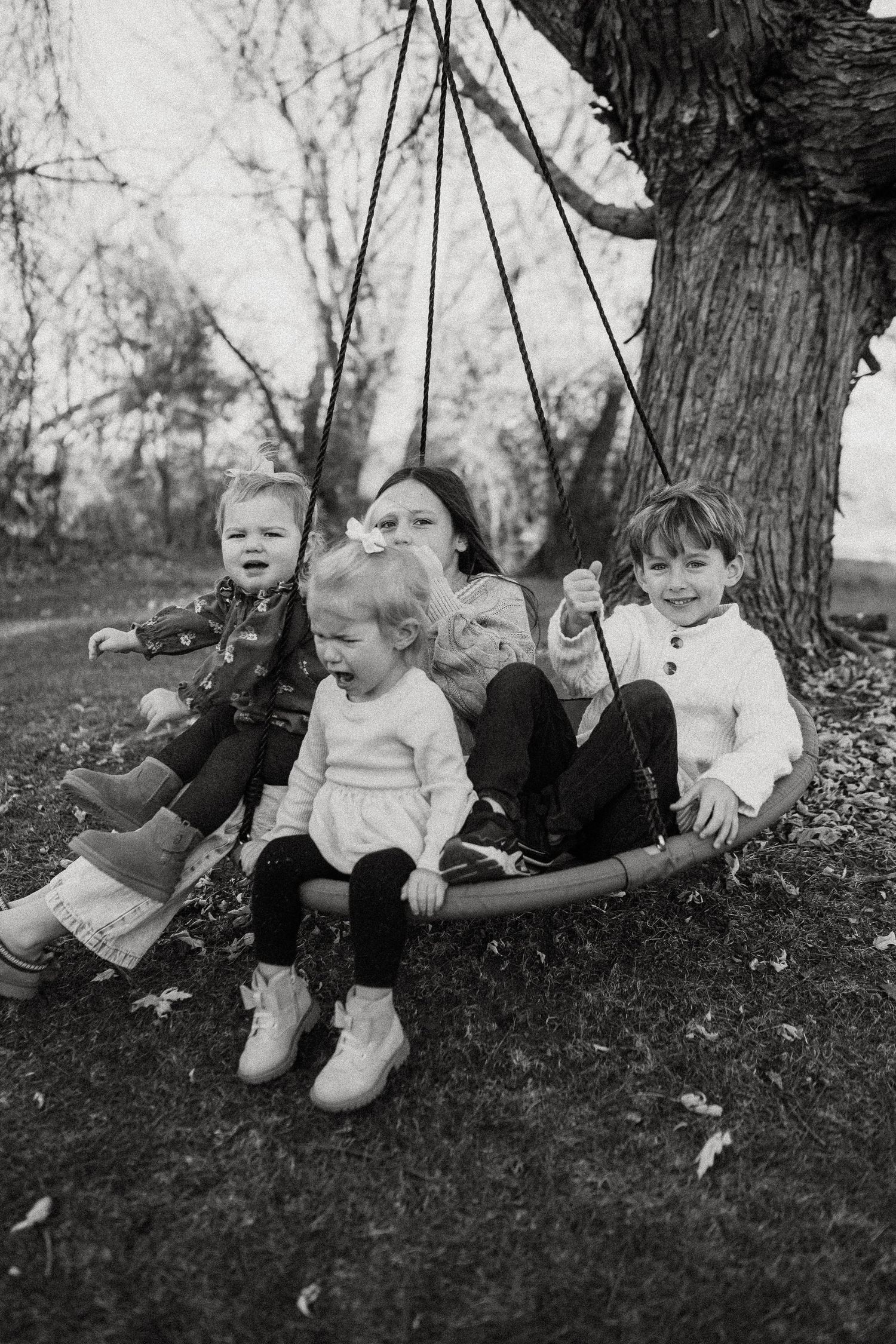 Children enjoy a playful moment together on a large tree swing in black and white photography.