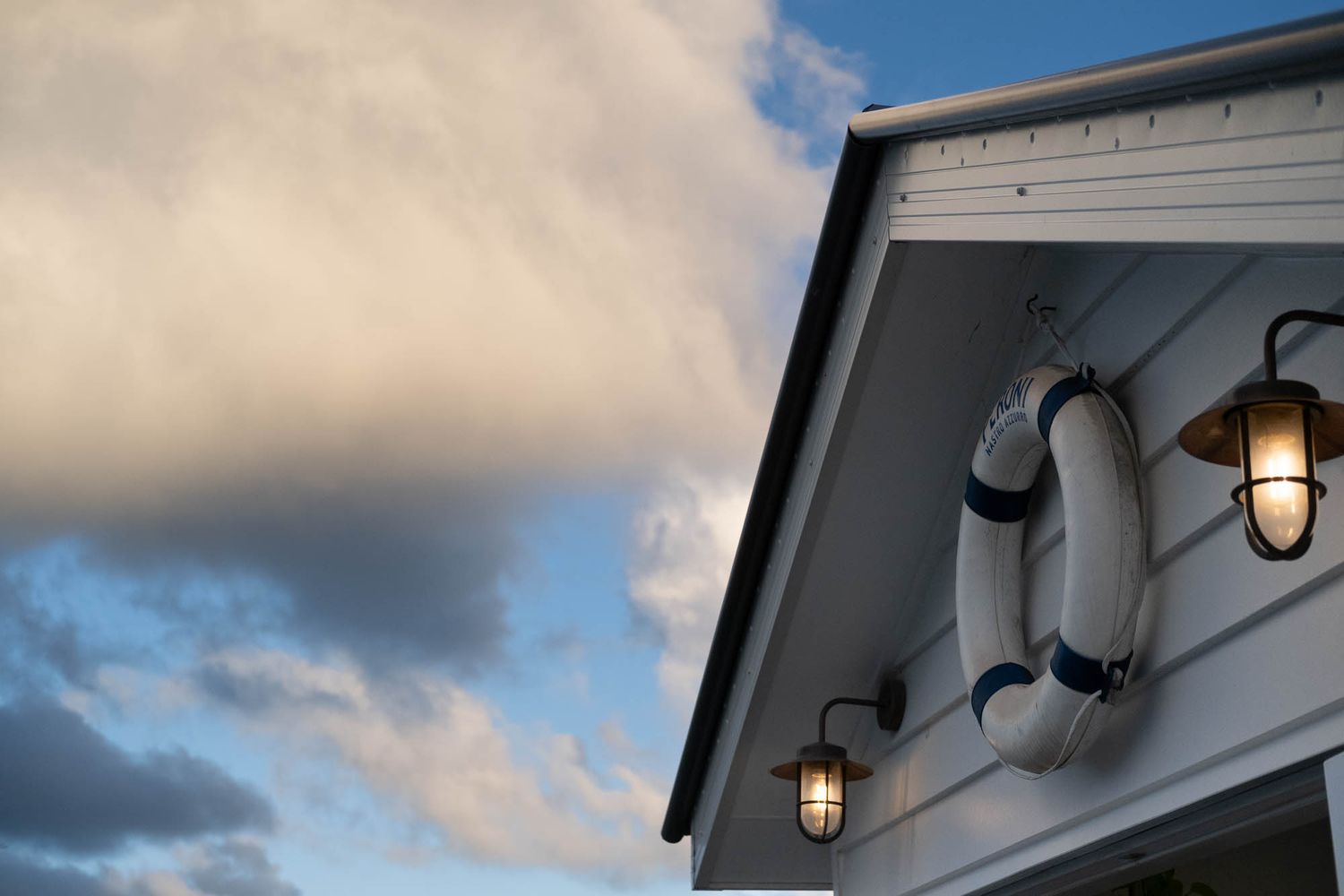 Sunshine Coast real estate photography: detail of a nautical pool house gable with lifebuoy decor and lit barn lights against a dusk sky