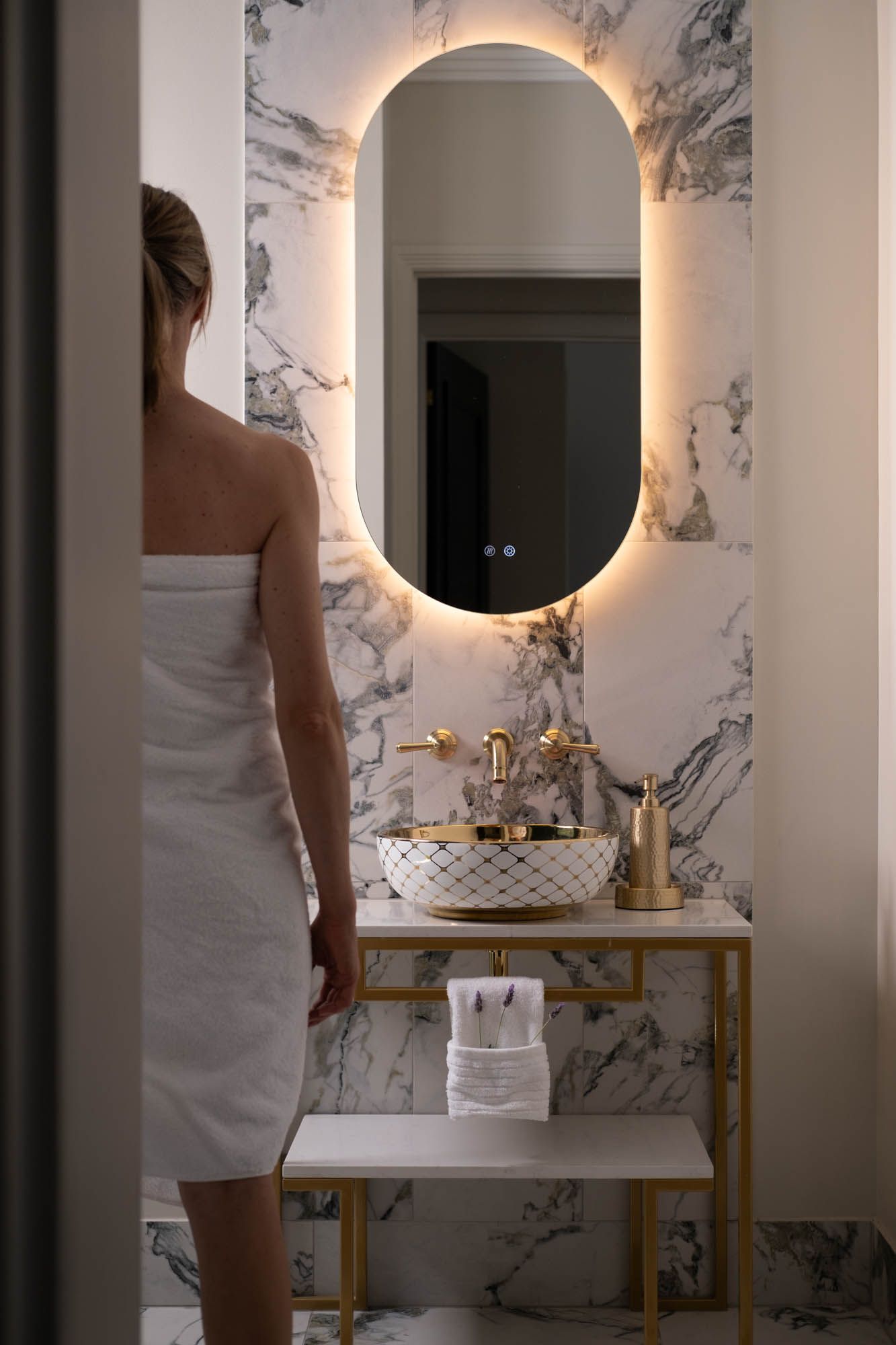 Sunshine Coast lifestyle photography: luxury marble bathroom with gold fixtures, backlit oval mirror, and premium patterned vessel sink.