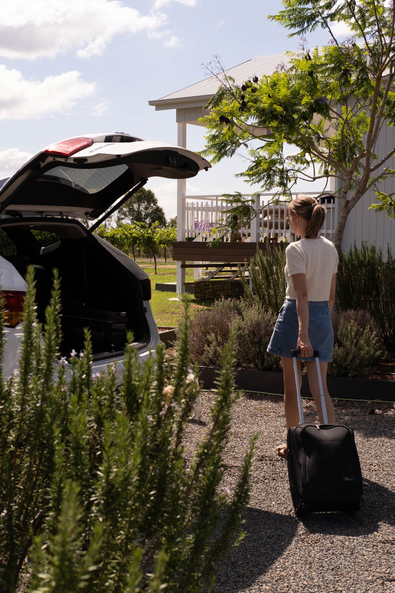 Sunshine Coast lifestyle photography: woman with suitcase by a white weatherboard cabin, highlighting holiday rental property potential