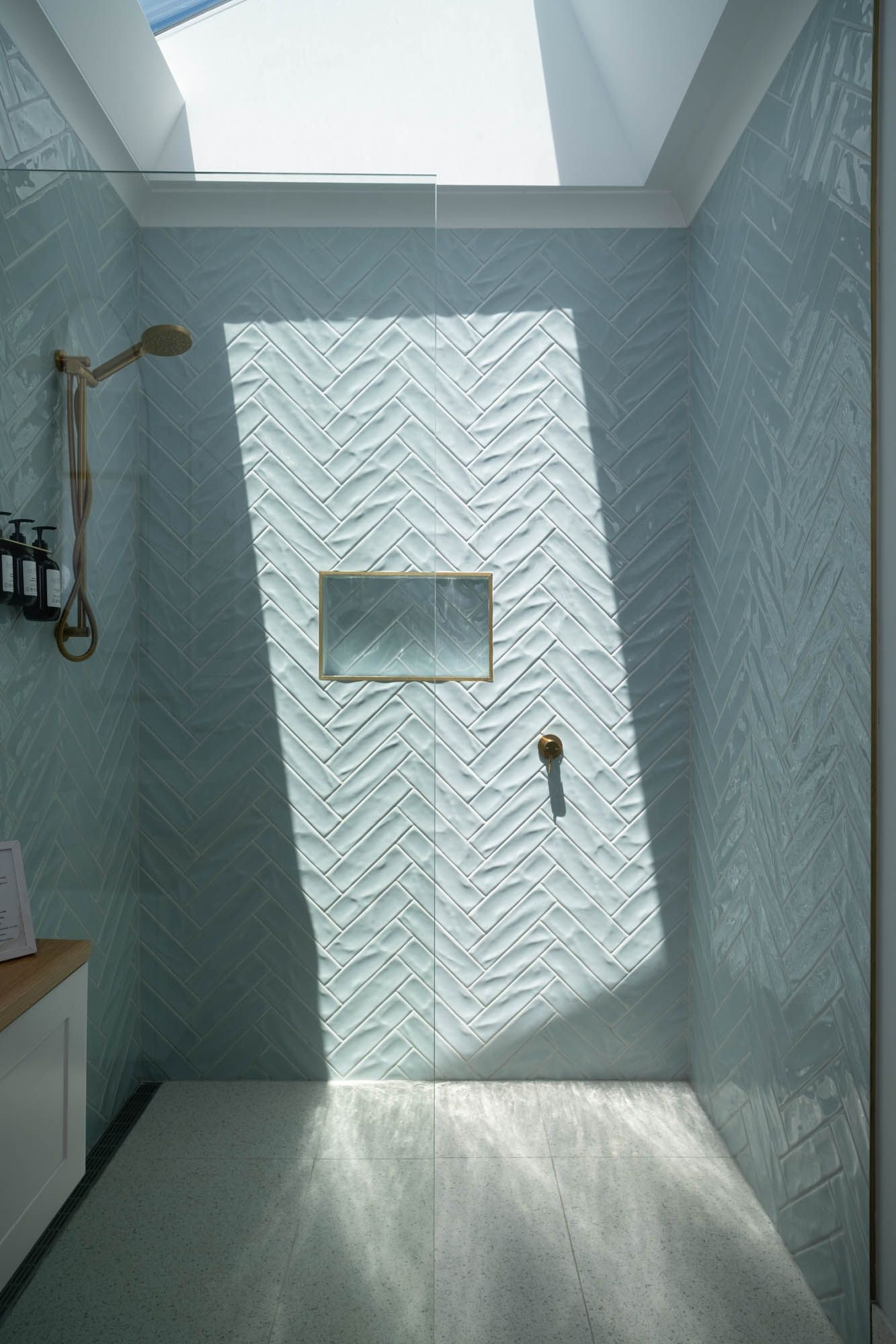 Sunshine Coast real estate photography: modern walk-in shower with light blue herringbone tiles, skylight, and luxury gold hardware