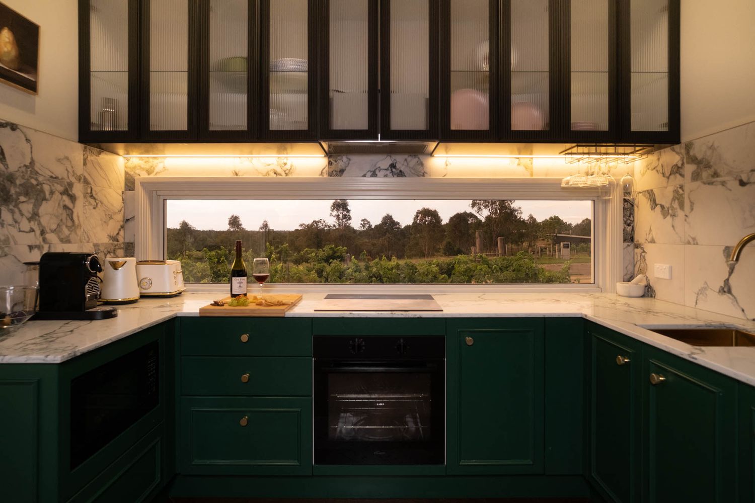 Sunshine Coast real estate photography: luxury kitchen with dark green cabinetry, marble counters, and panoramic window view of a vineyard.