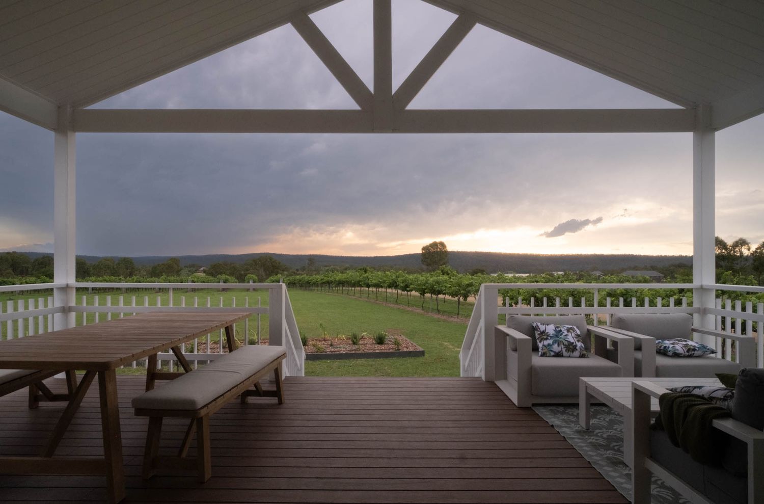 Sunshine Coast real estate photography: luxury cabin deck at sunset with a timber dining set, lounge chairs, and a scenic vineyard view