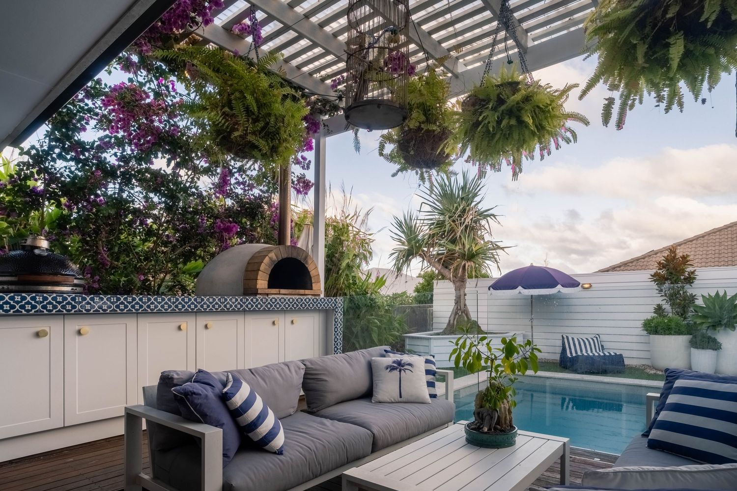 Sunshine Coast real estate photography: luxury outdoor entertaining area with a pizza oven, grey lounge seating, and a swimming pool view