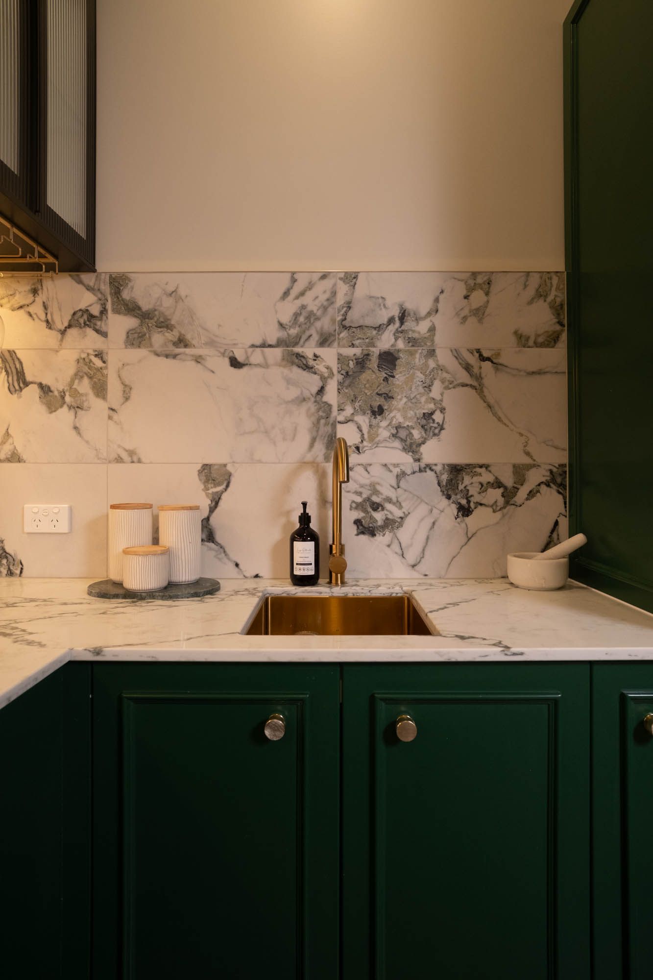 Sunshine Coast real estate photography: luxury kitchen with dark green cabinetry, marble backsplash, and premium gold sink and tapware.