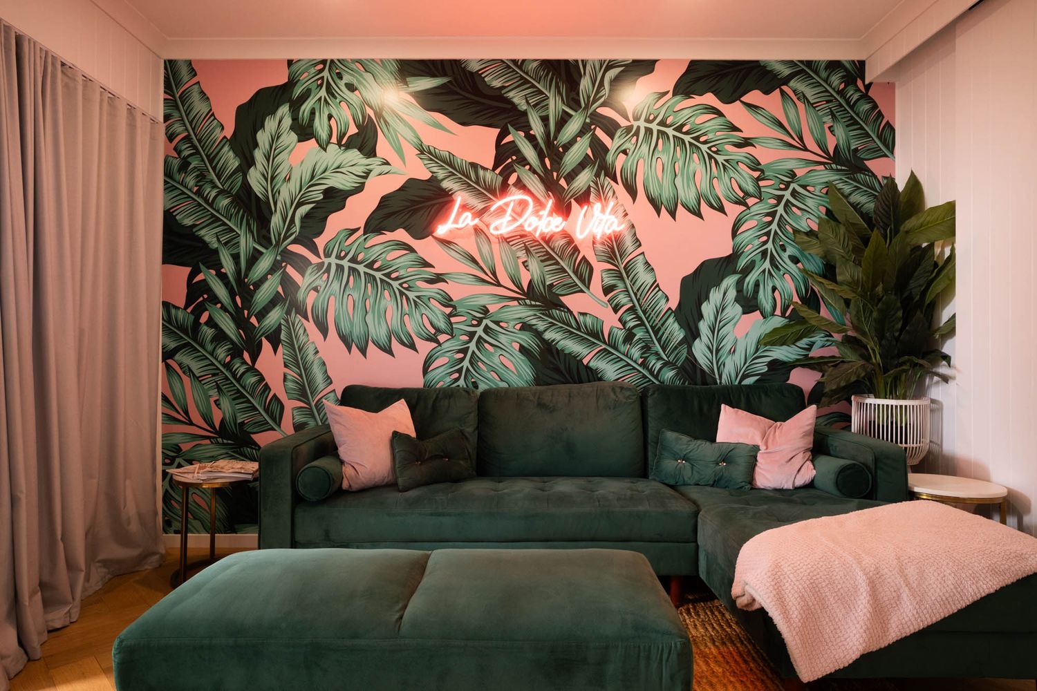 Sunshine Coast lifestyle photography: maximalist living room with palms on pink wallpaper, green velvet sofa, and 'La Dolce Vita' neon sign.