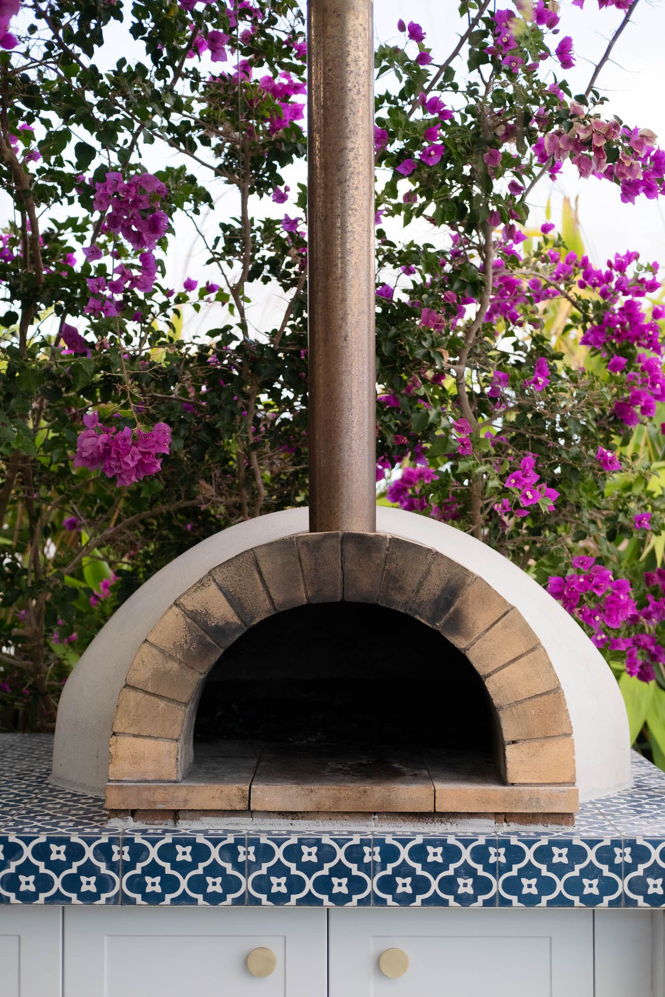 Sunshine Coast real estate photography: close-up of a luxury outdoor wood-fired pizza oven with blue mosaic tile and bougainvillea
