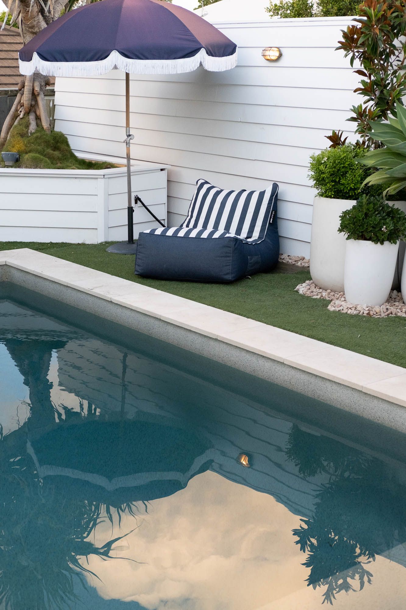 Sunshine Coast lifestyle photography: luxury poolside lounging area with striped bean bag, fringed umbrella, and white coastal fencing