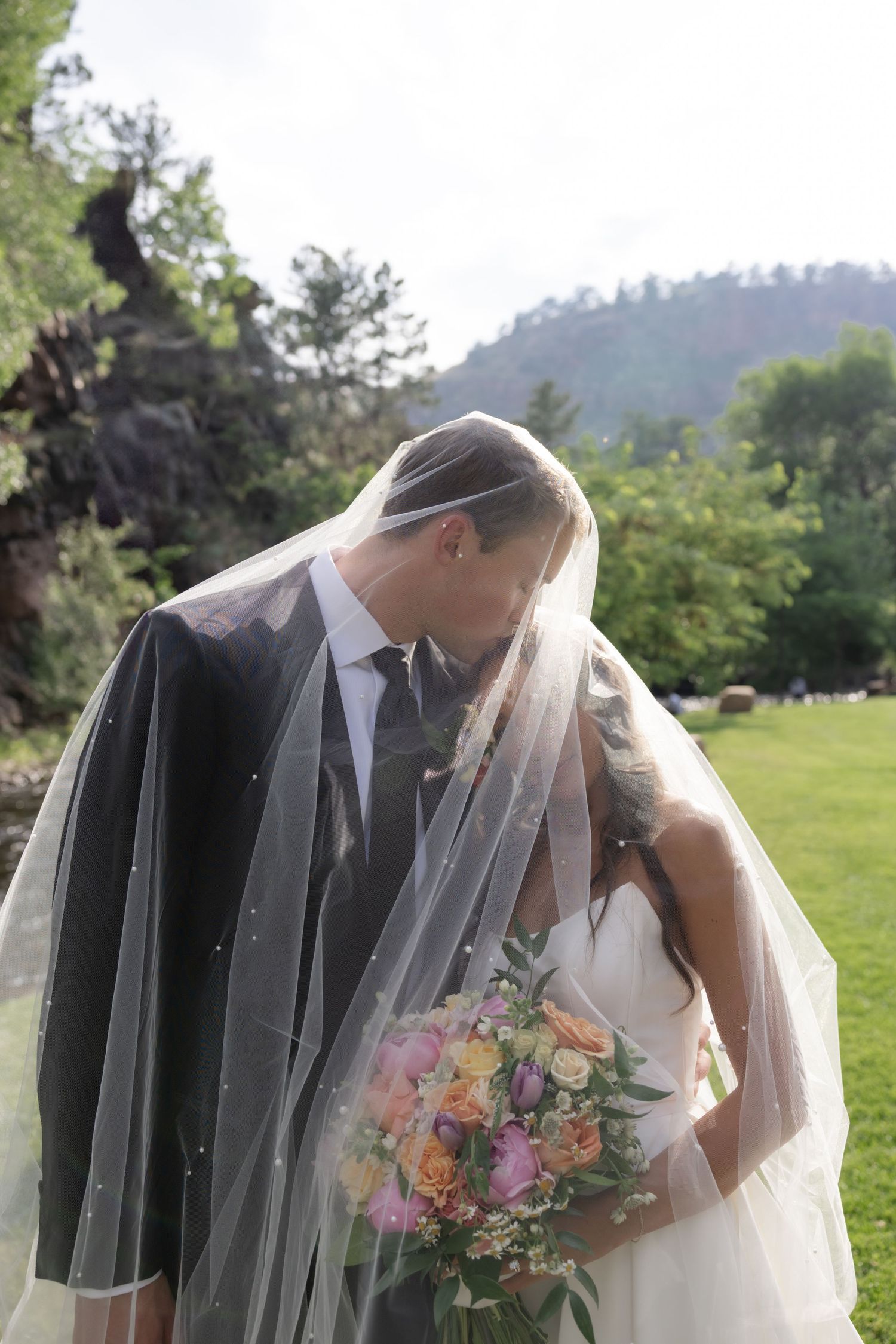 Intimate wedding moment captured under flowing white veil in garden setting.