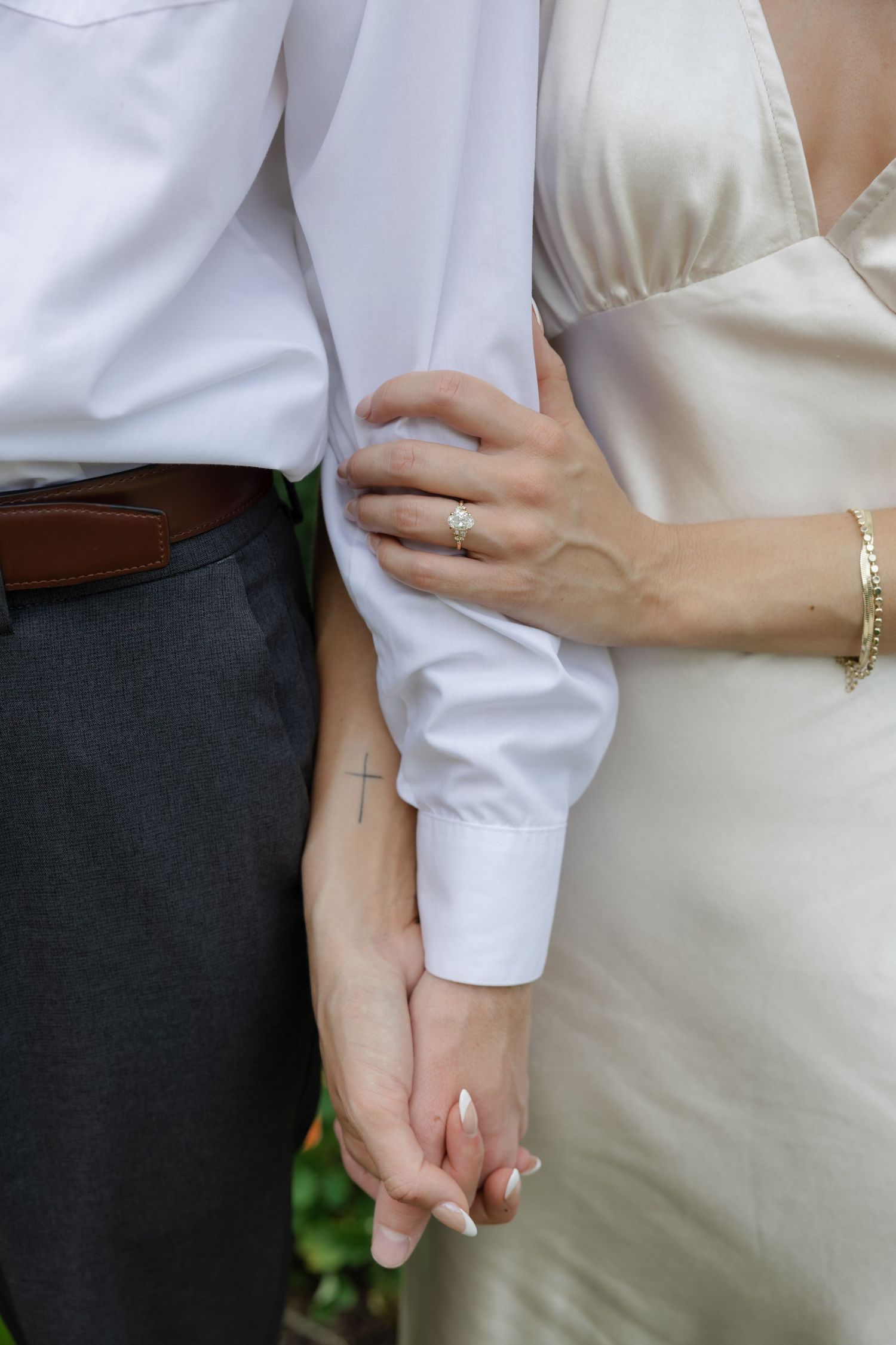 Close up detail of a couple holding hands showing wedding rings and formal attire.