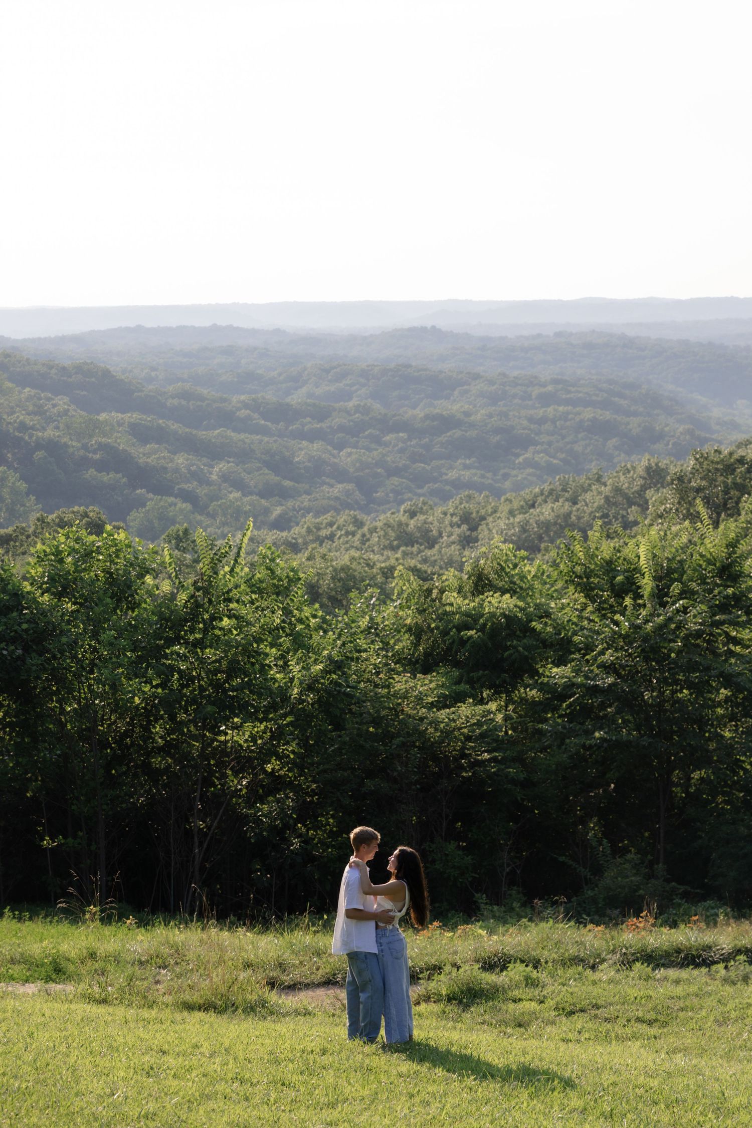 A panoramic view of a couple's intimate moment in a vast hillside meadow.
