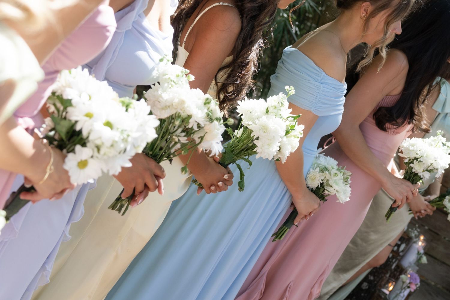 Bridesmaids holding white floral bouquets while wearing soft pastel colored dresses.