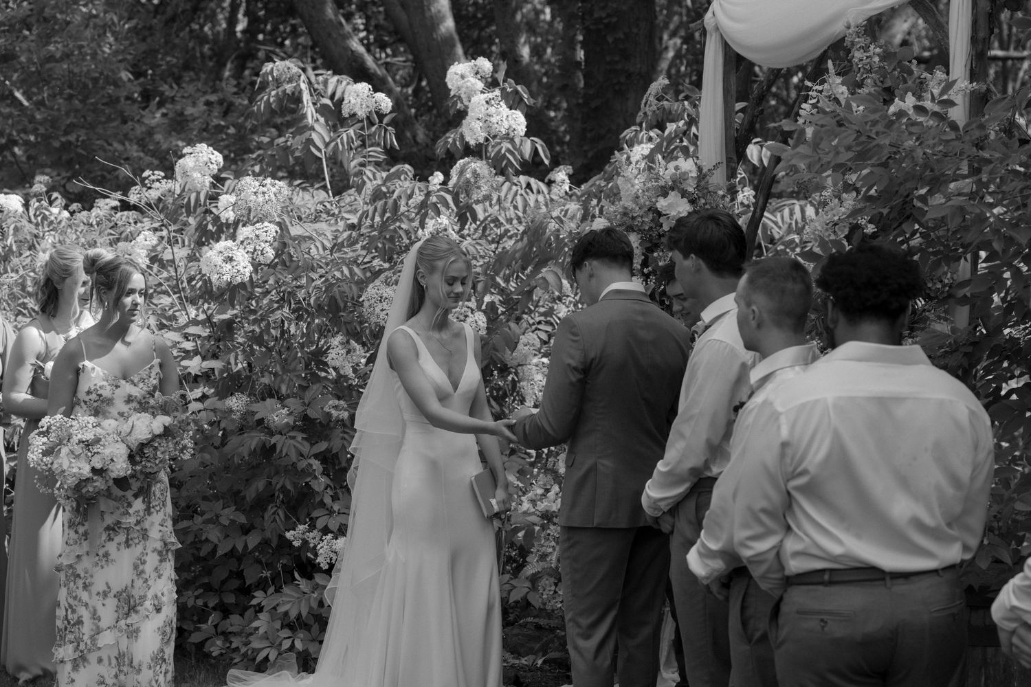 Wedding ceremony taking place under trees with white decorations and floral arrangements.