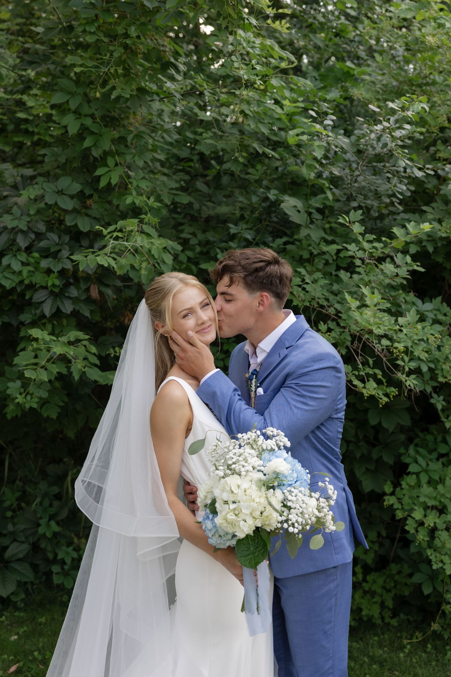 Intimate wedding portrait moment among green summer foliage.