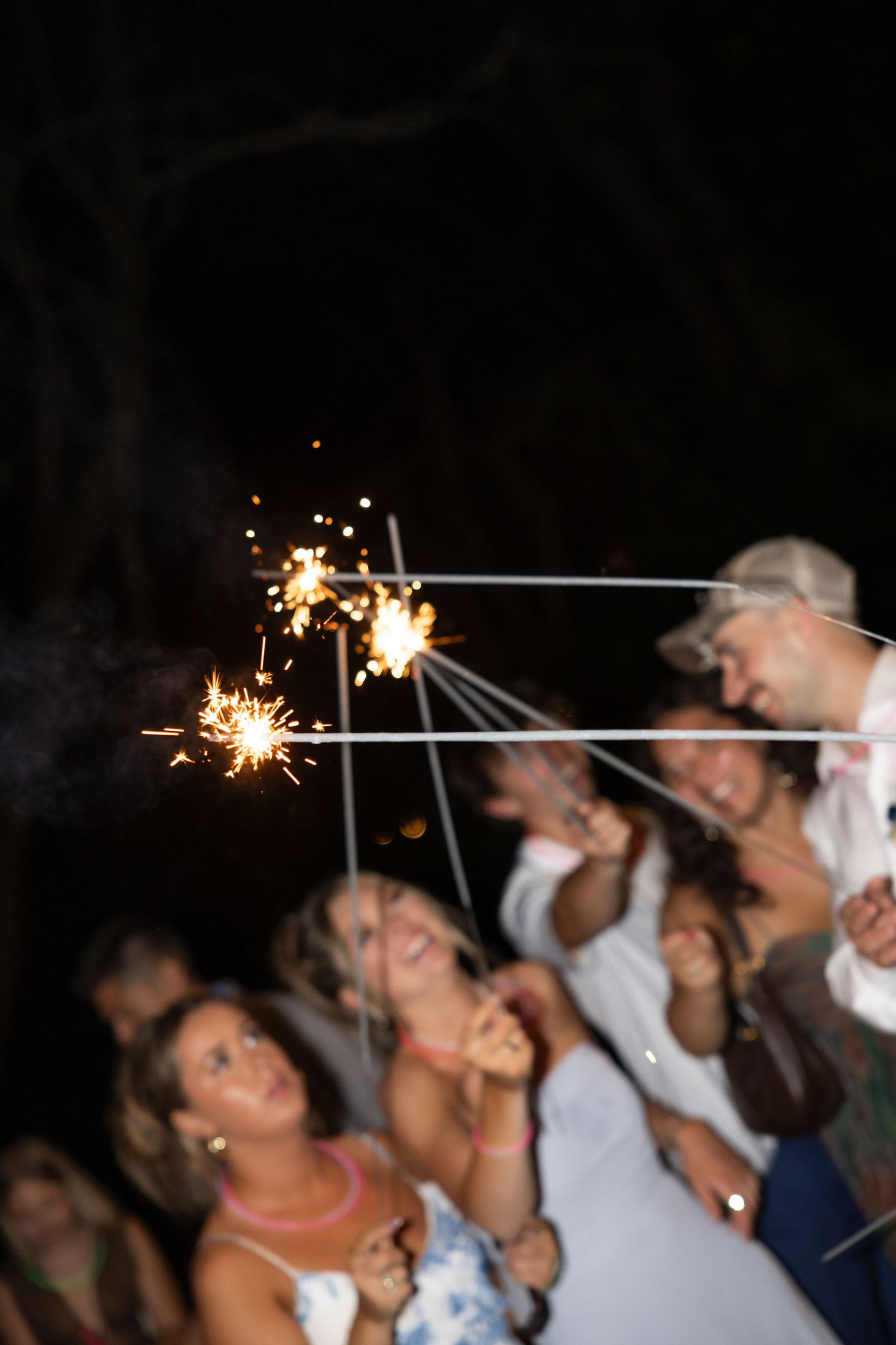 Party guests hold sparklers up in the night sky during an outdoor celebration.