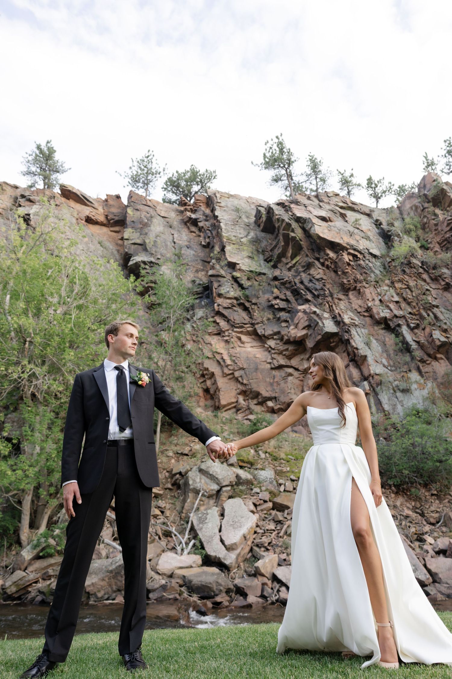 Newlyweds hold hands against a dramatic rocky cliff backdrop in an outdoor wedding setting.