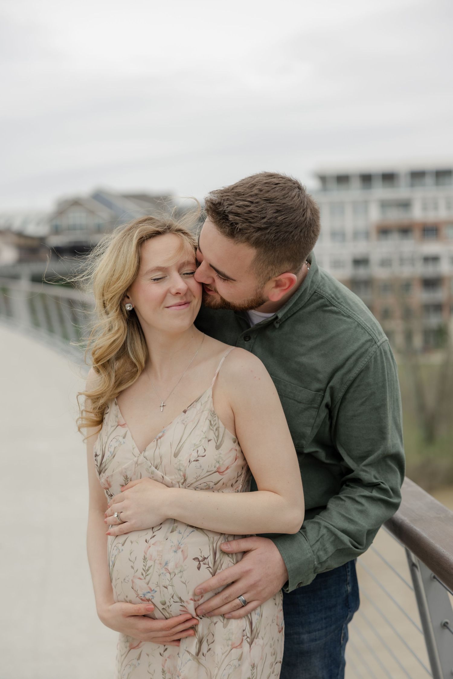 Expecting couple embracing tenderly on an outdoor bridge during maternity photoshoot.