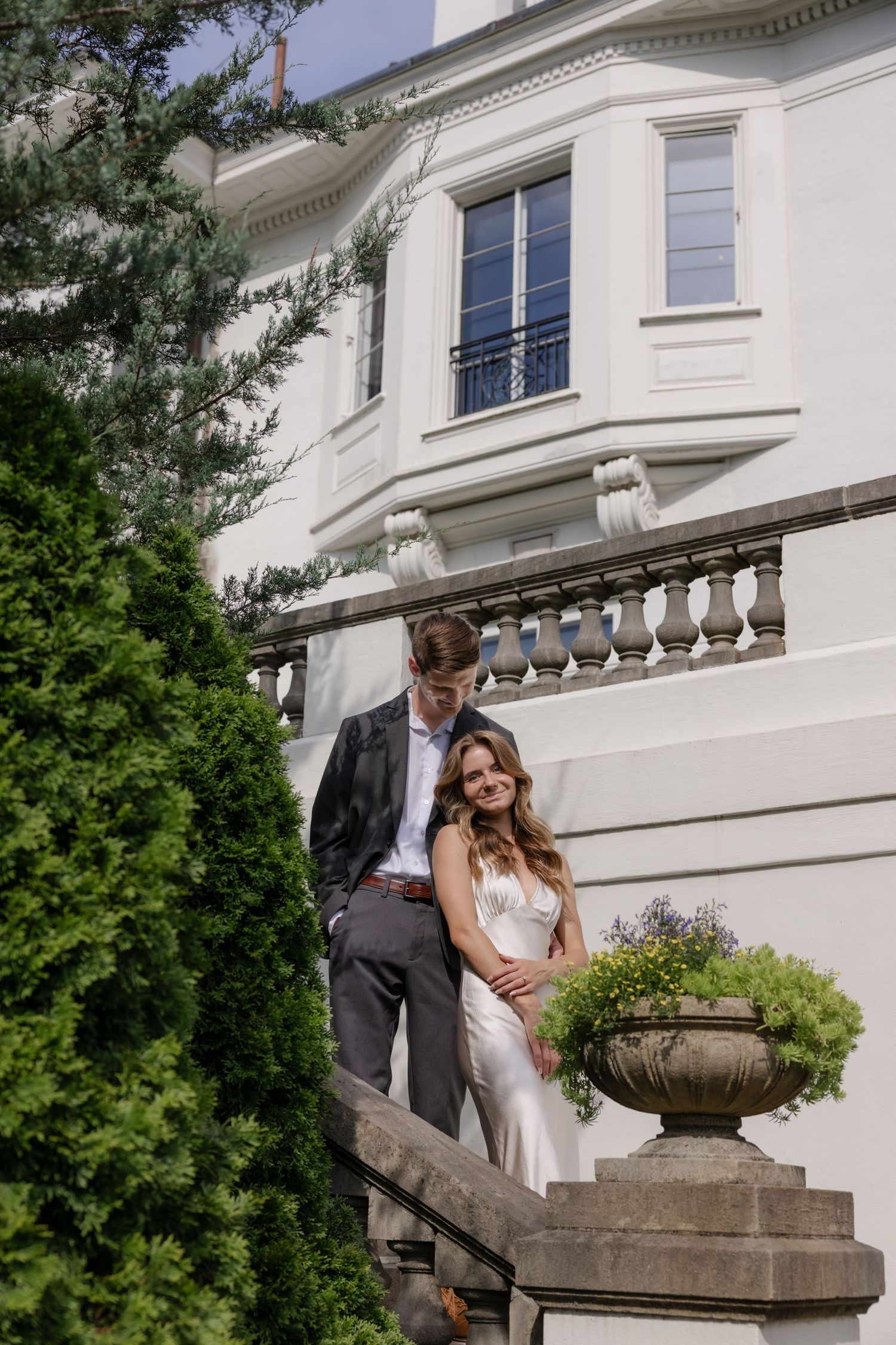 Couple standing together on stone steps in front of elegant white mansion building.