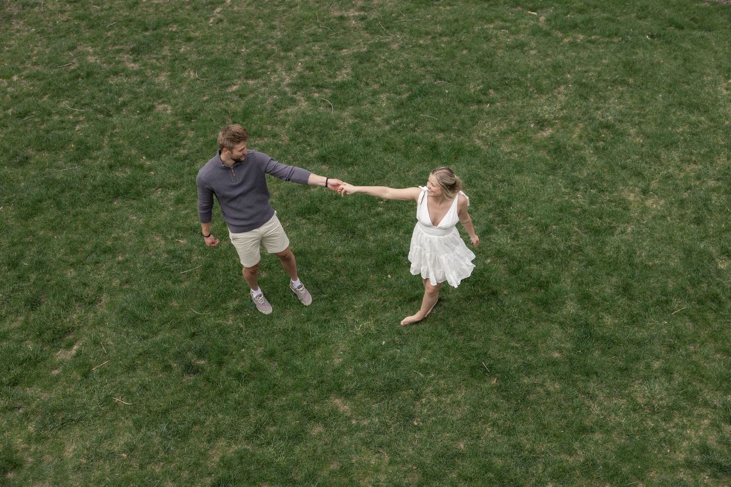 Aerial drone shots show a couple walking and dancing together on grass.