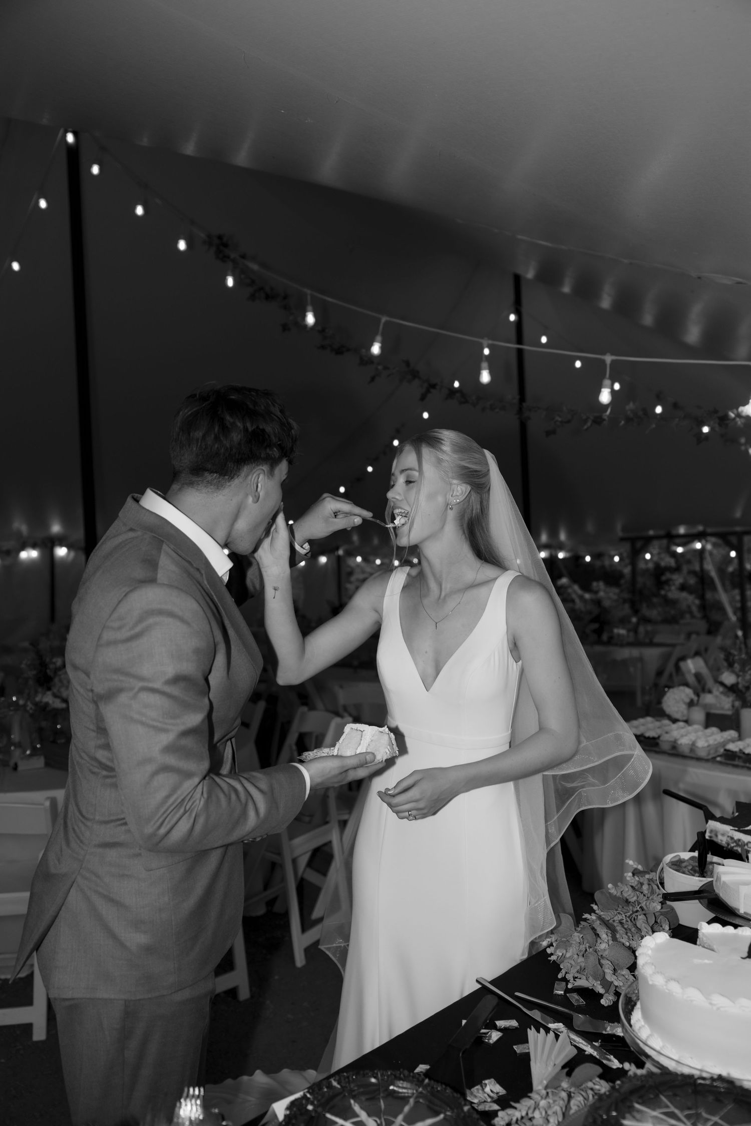 Black and white photo of newlyweds playfully feeding each other wedding cake.