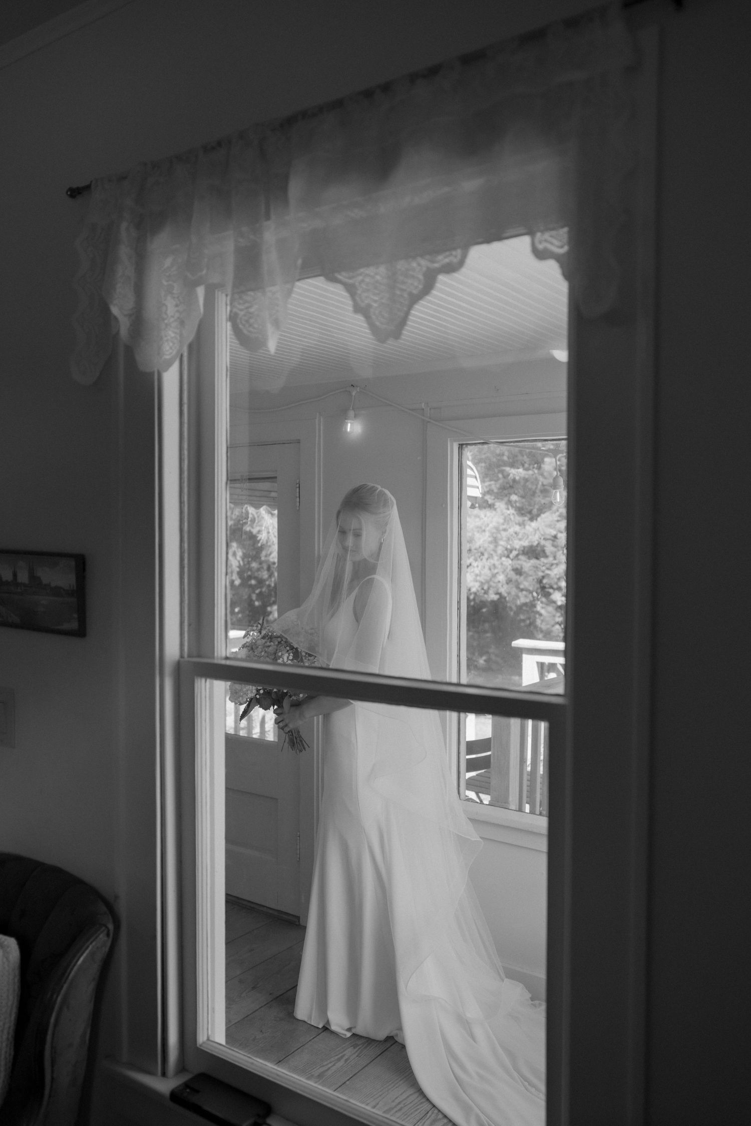 Black and white image showing a white wedding dress silhouetted in a window.