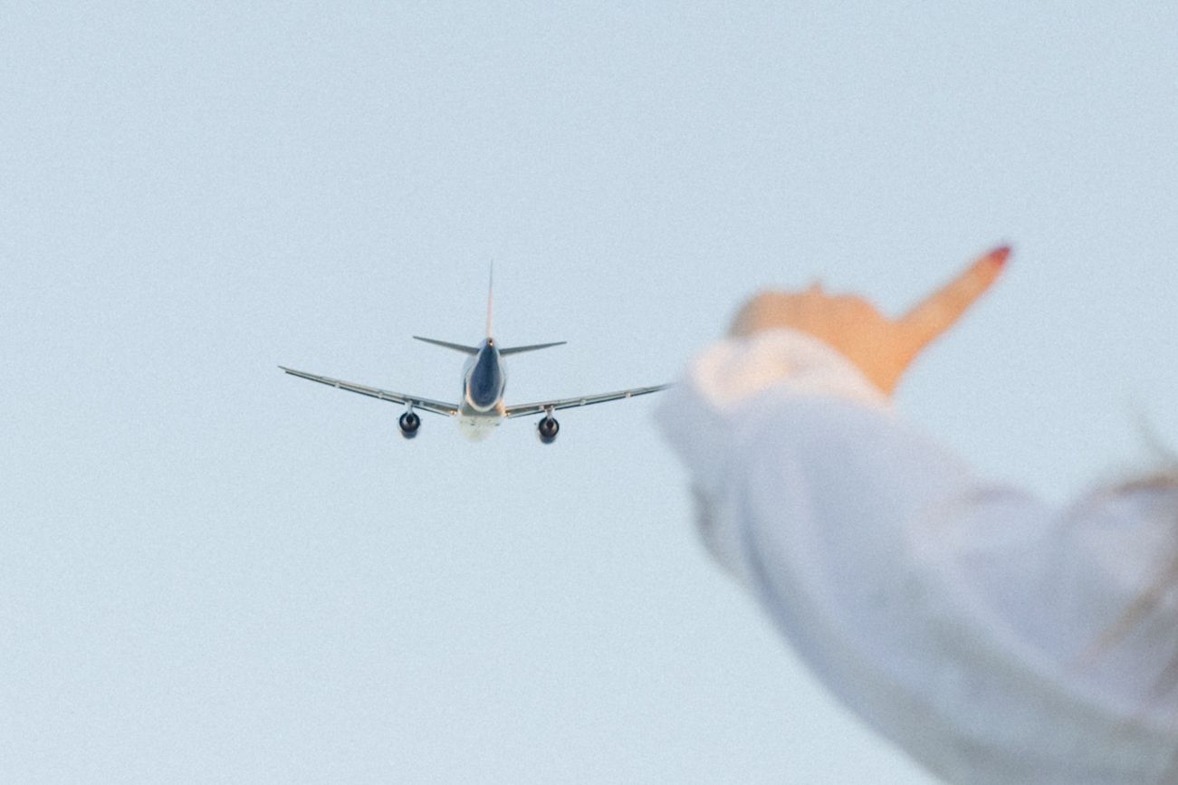 Silhouette of airplane against light blue sky with person's hand waving.