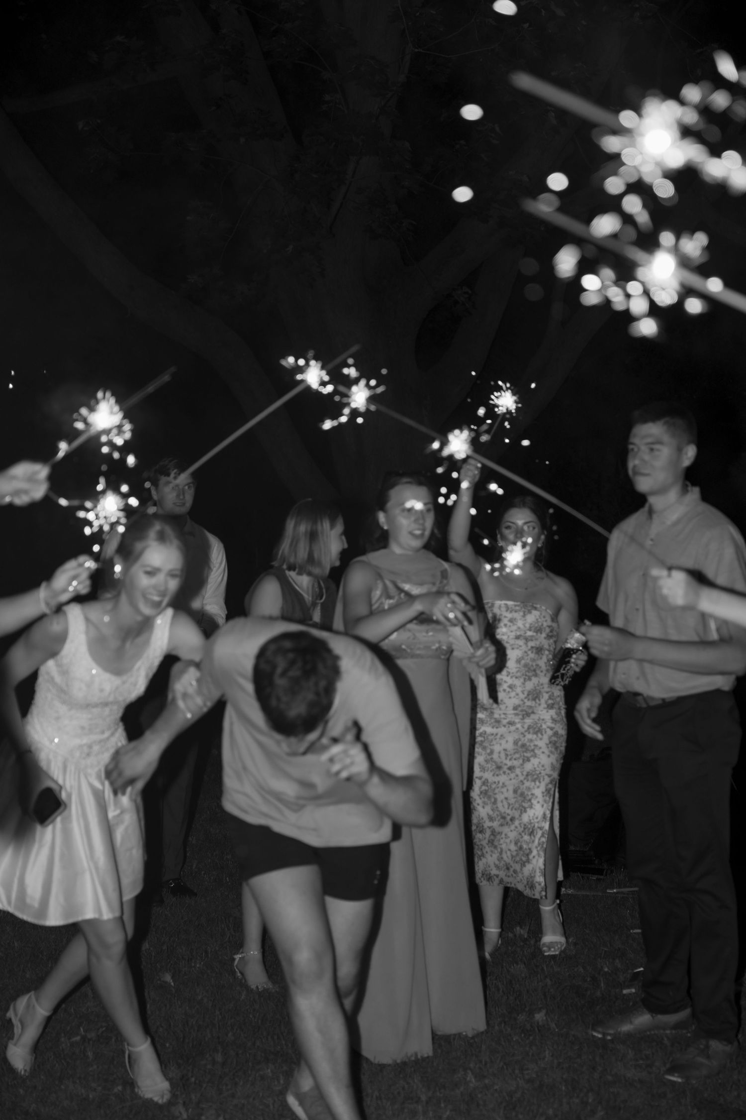 Party guests dance and pose while holding sparklers during a night celebration.