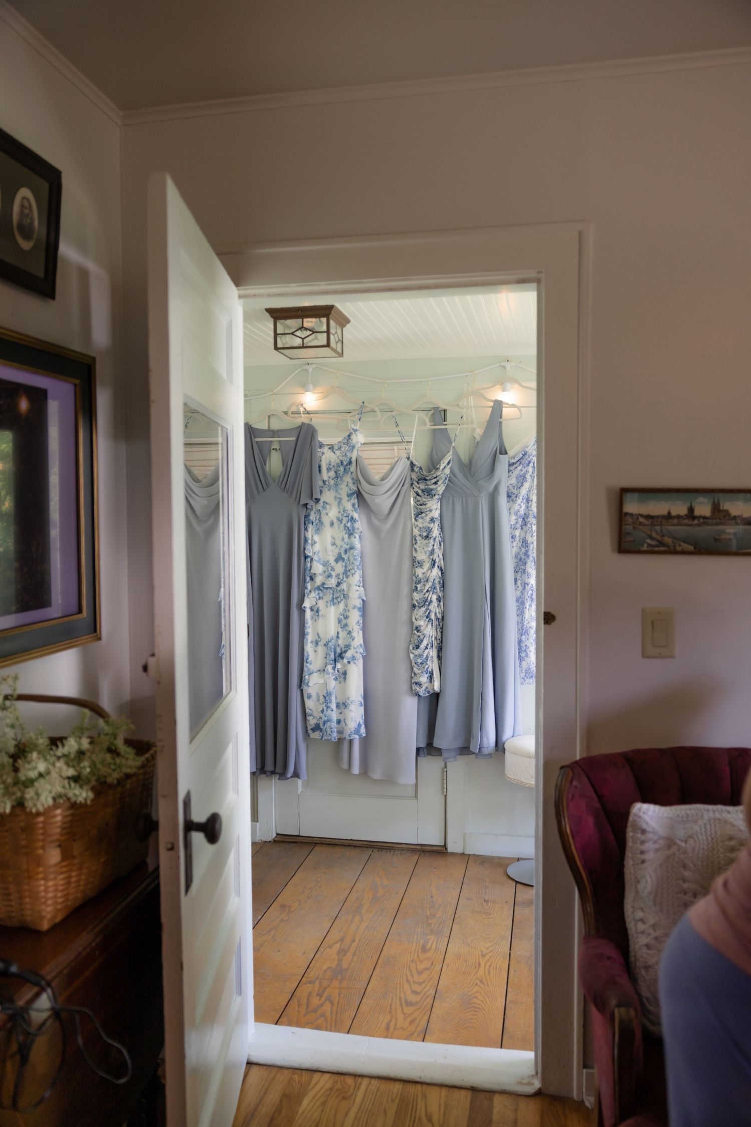 Light blue bridesmaid dresses hanging in a sunlit hallway with wooden floors.