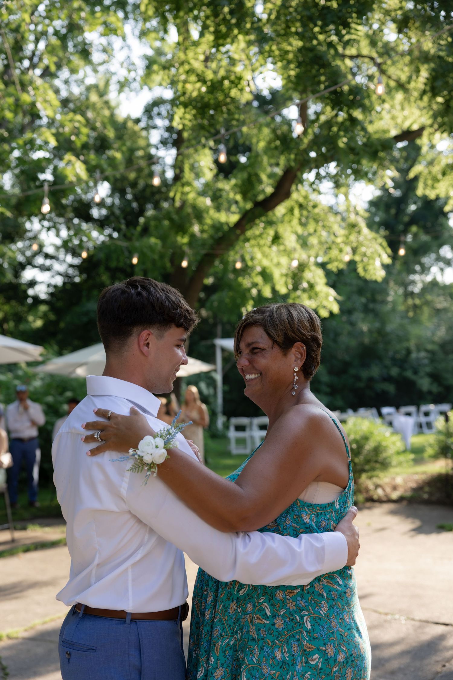 A touching dance moment shared beneath green trees at an outdoor wedding celebration.