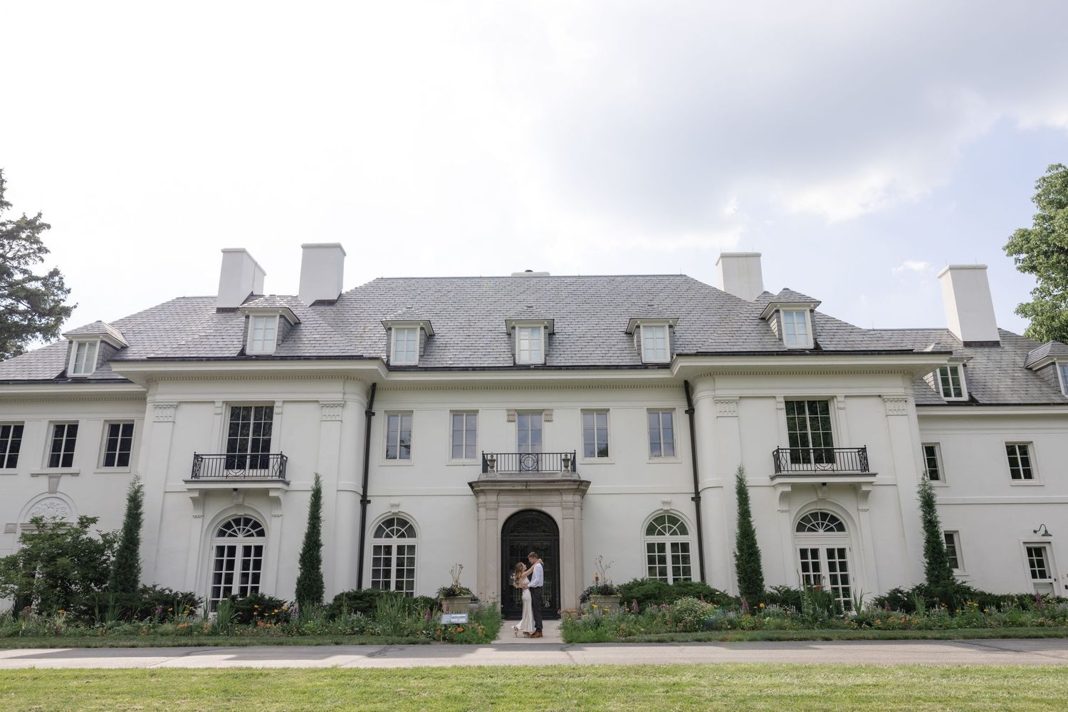 Grand white mansion with classical architecture and multiple dormer windows stretches across the frame.