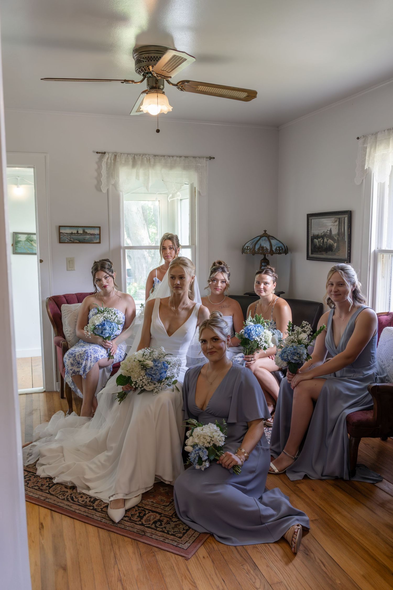 Wedding party relaxing indoors with bridesmaids in gray dresses and bride on comfortable furniture.