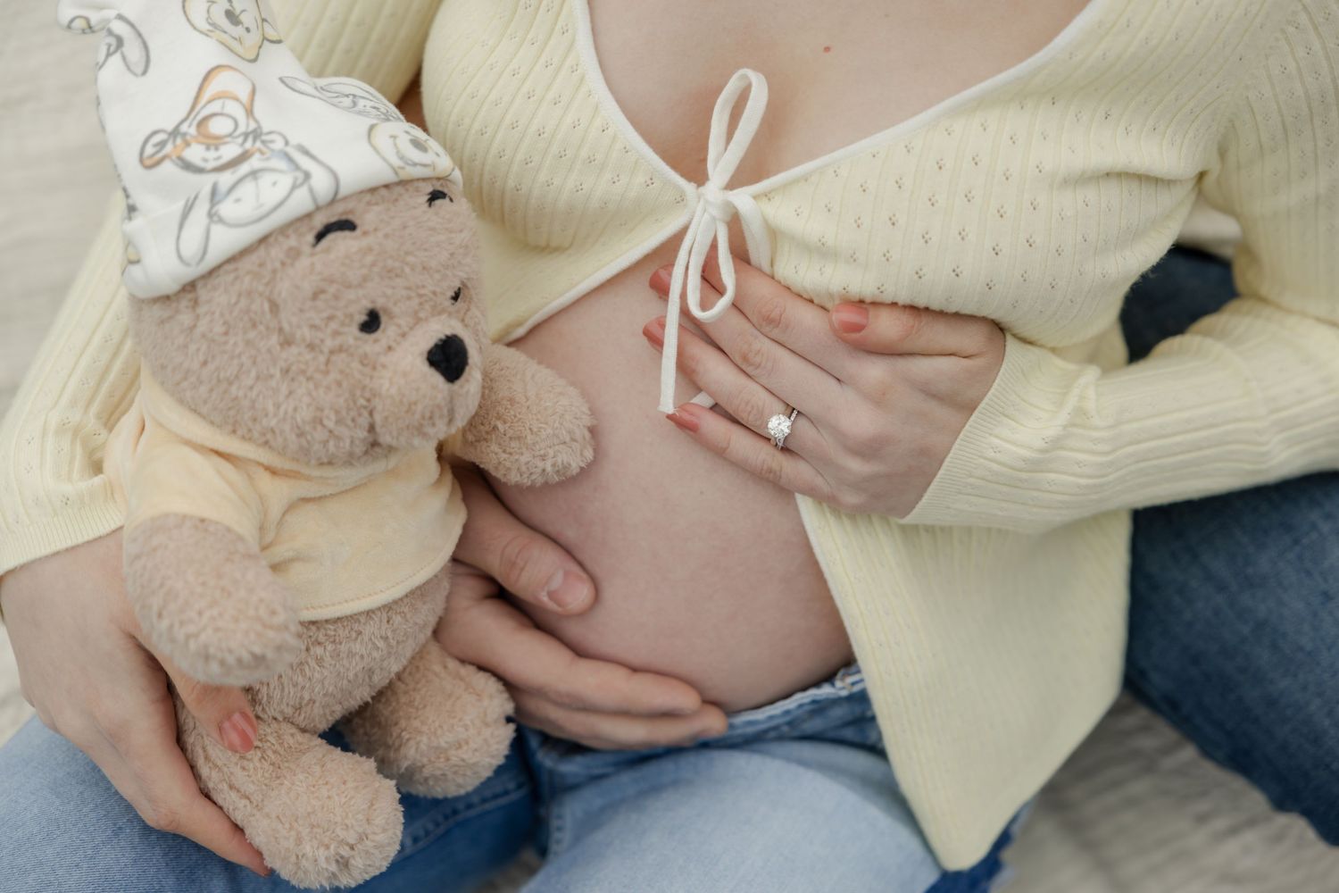 Close up of pregnant belly with teddy bear wearing matching patterned hat.